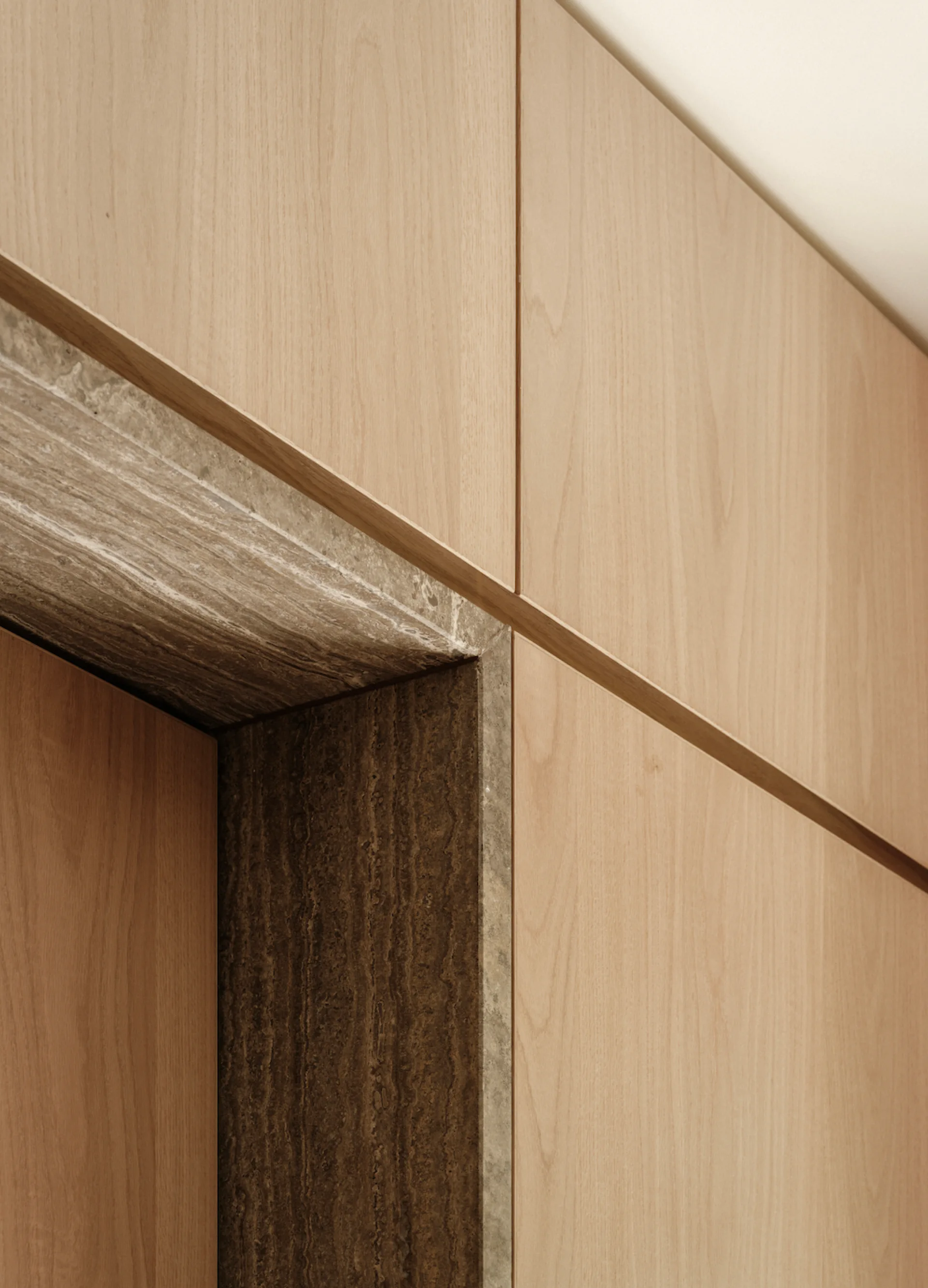 A close-up view of flush light wood wall panels fitted against a recessed entryway lined with textured dark brown stone.