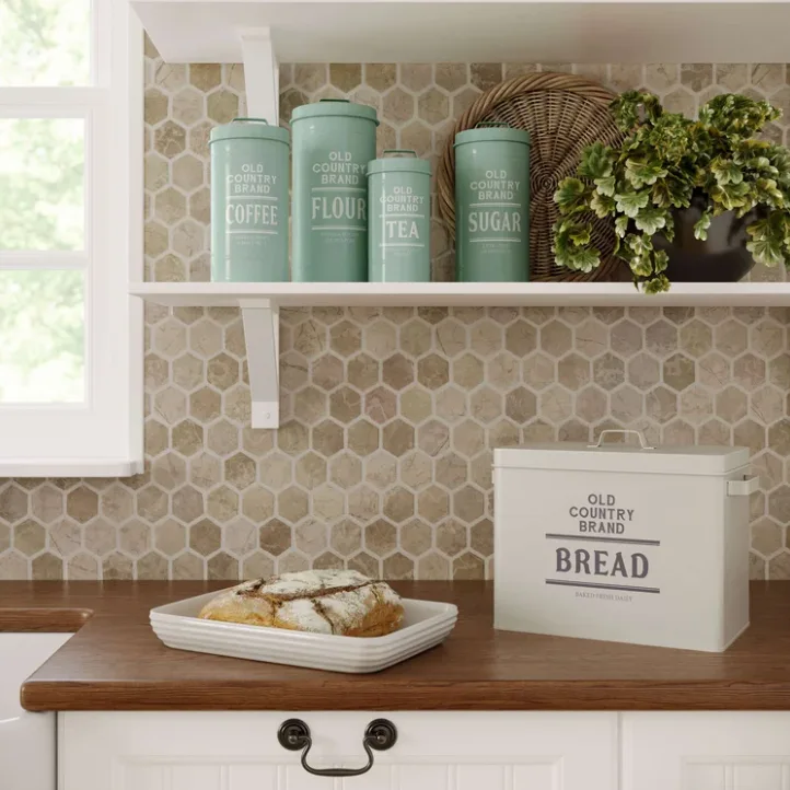 A kitchen counter features a wooden countertop, a stone hexagon tile backsplash, and vintage-style aqua canisters on a white floating shelf.