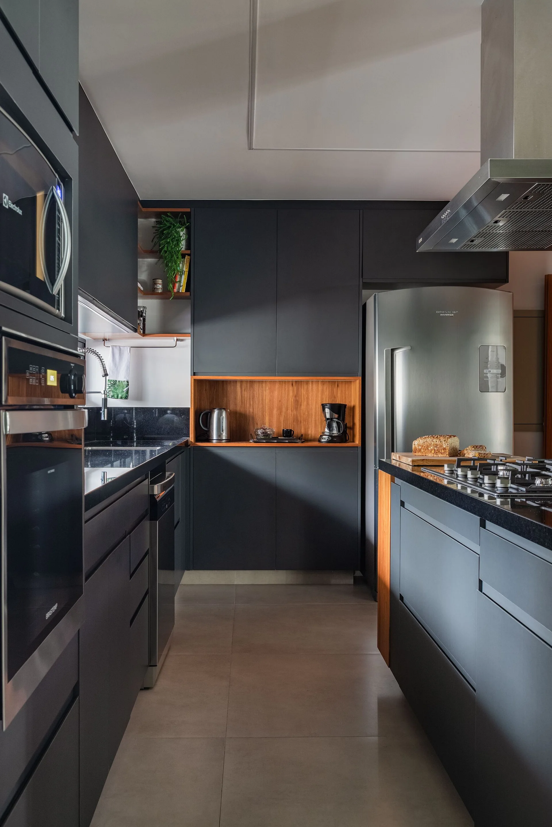 A modern kitchen featuring matte dark grey cabinetry, a built-in wood-toned display niche, stainless steel appliances, and black countertops.