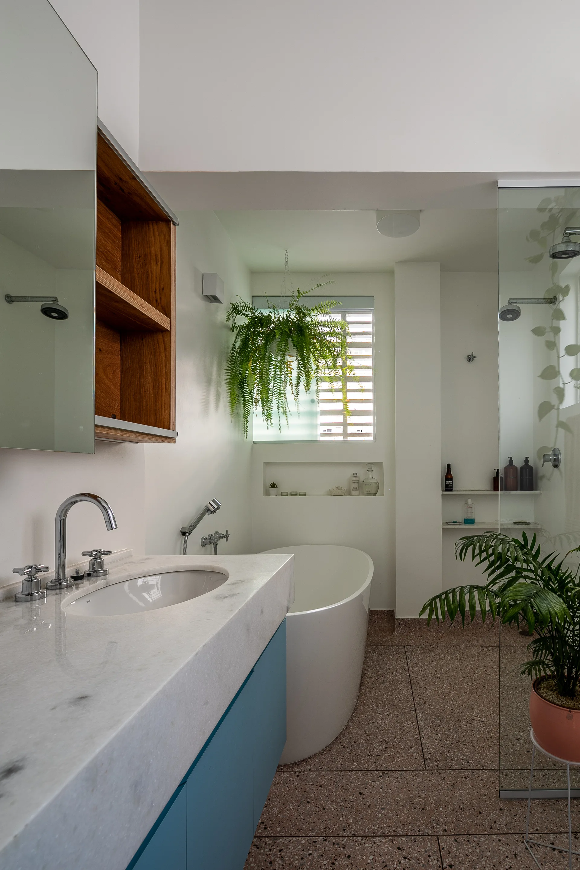 A modern bathroom featuring a blue vanity with a stone countertop, a white freestanding bathtub, and speckled terrazzo flooring.