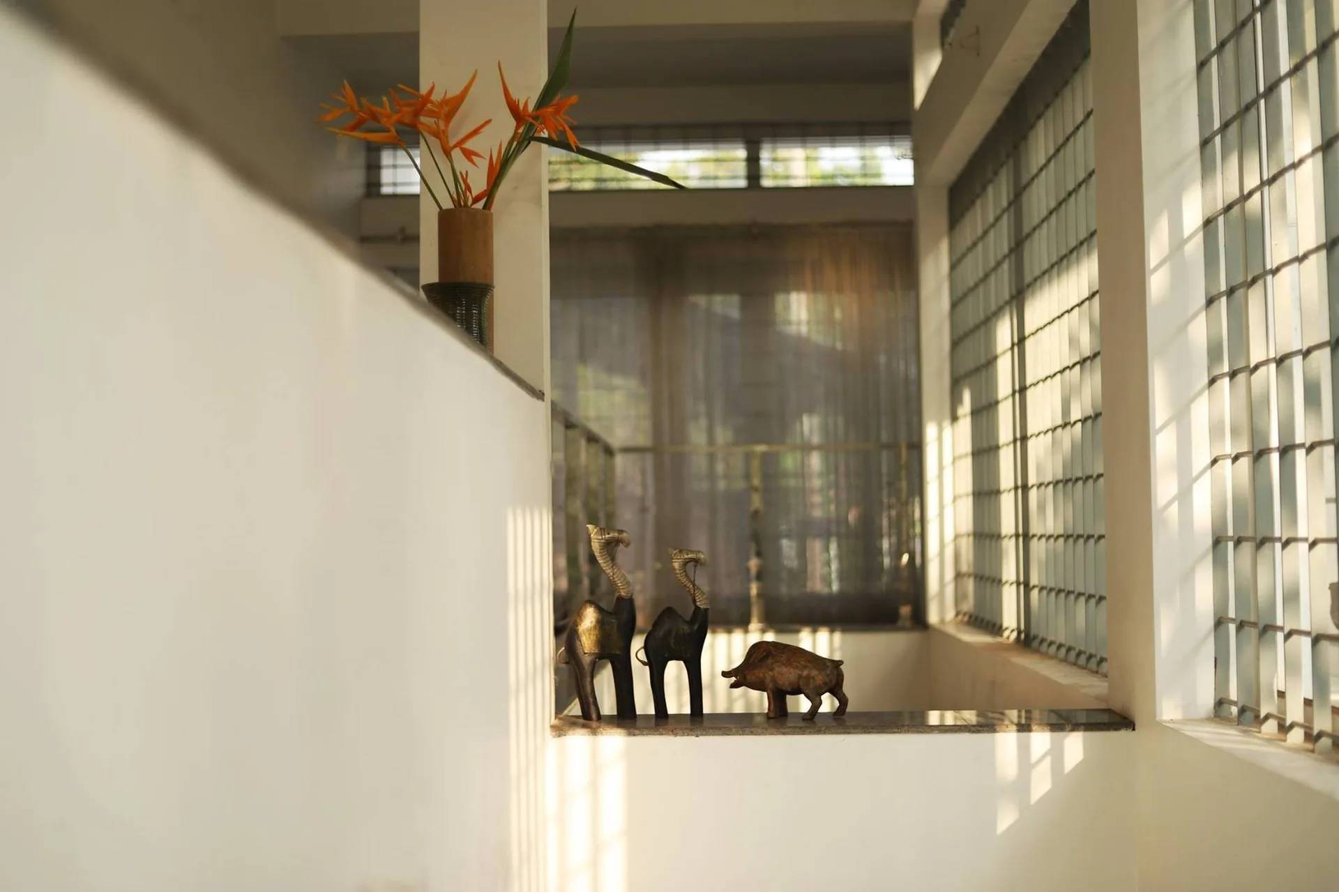 Small bronze animal sculptures sit on a white wall ledge of a bright stair landing under grid-patterned window shadows.
