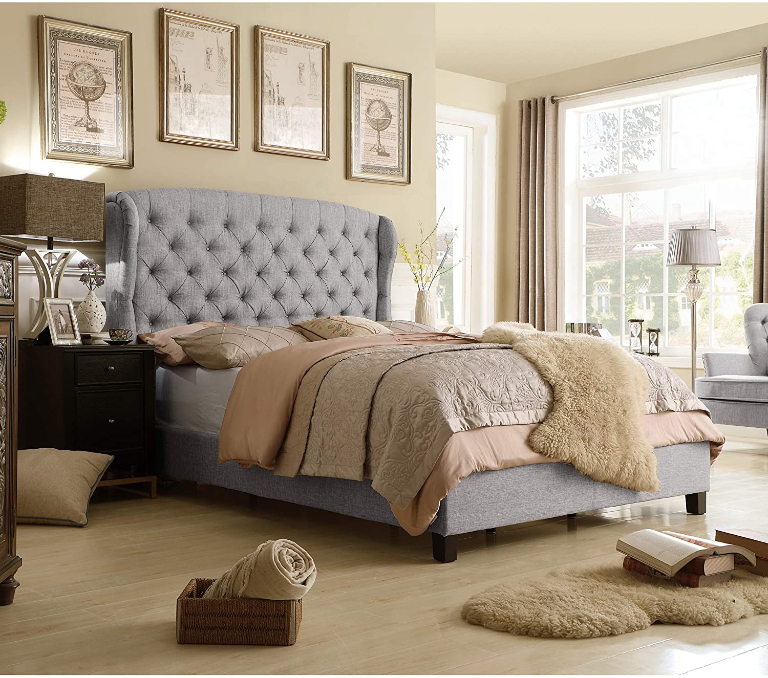 A bedroom with a grey tufted wingback bed, light brown wood floors, and a horizontal row of four framed prints on the tan wall.