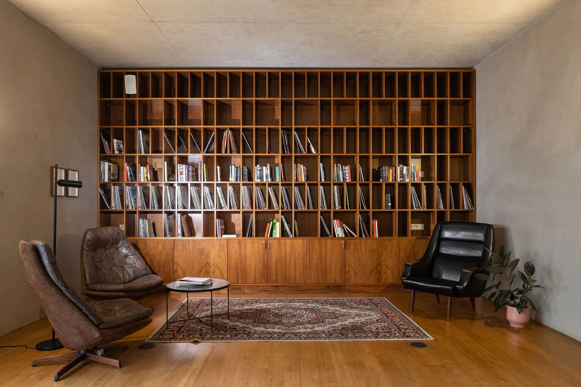 A home library features a large wooden floor-to-ceiling bookcase, two leather armchairs, a round coffee table, and an oriental rug on a wood floor.