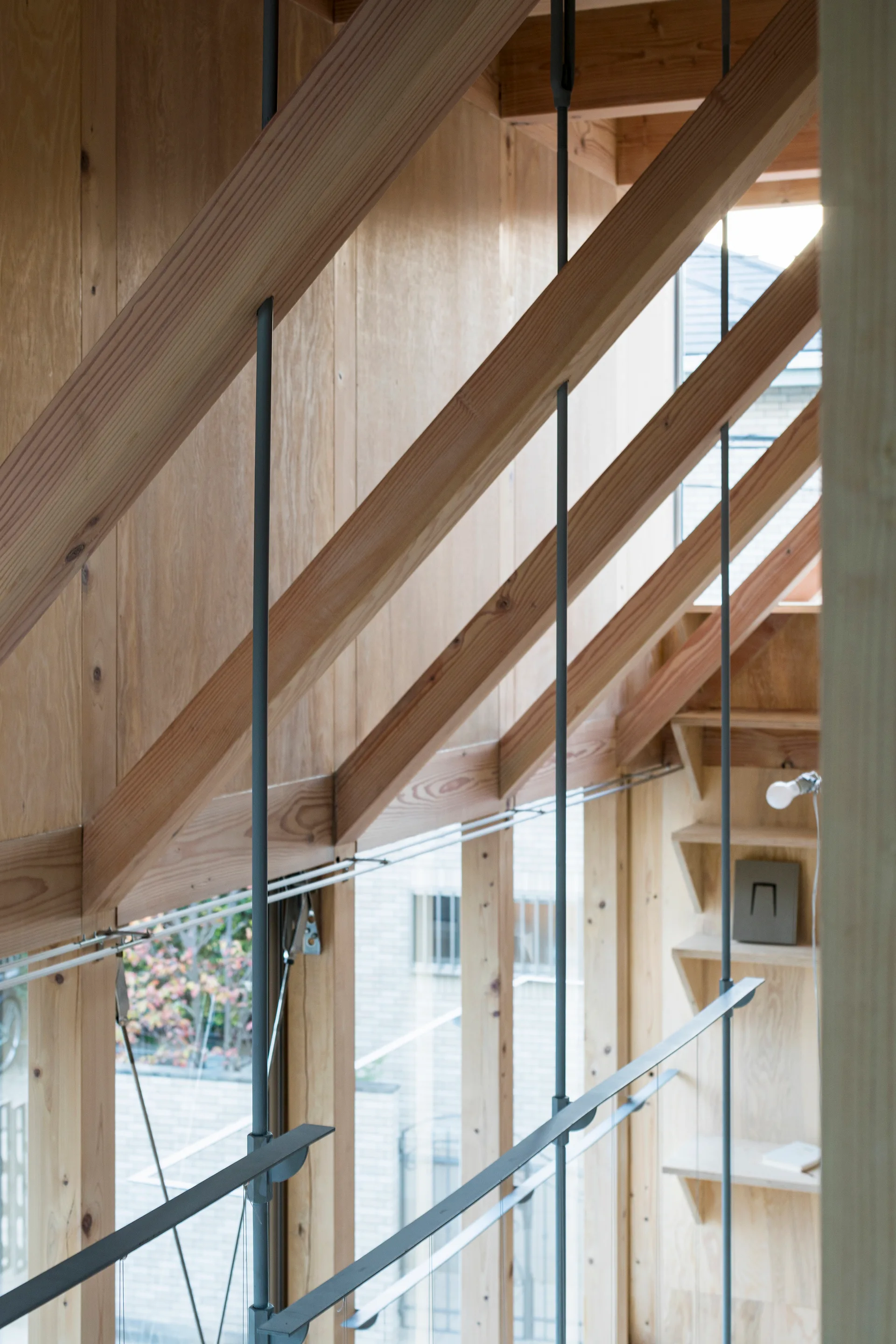 An interior view of a modern wooden home featuring exposed timber ceiling beams, light-colored plywood walls, and slim metal railing rods.