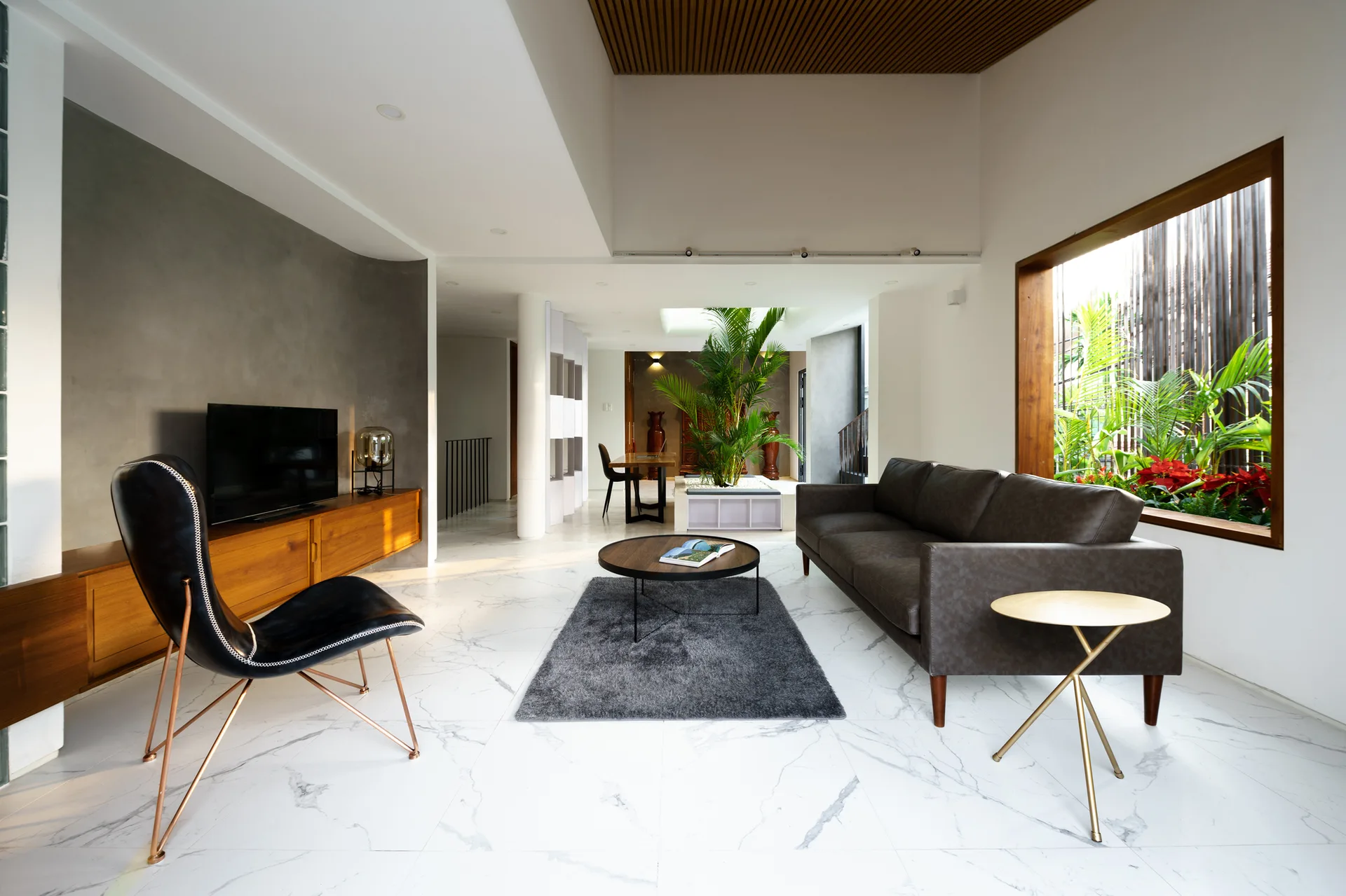 A modern living room with polished marble flooring, a grey concrete accent wall, a dark leather sofa, and a wood-slatted ceiling detail.