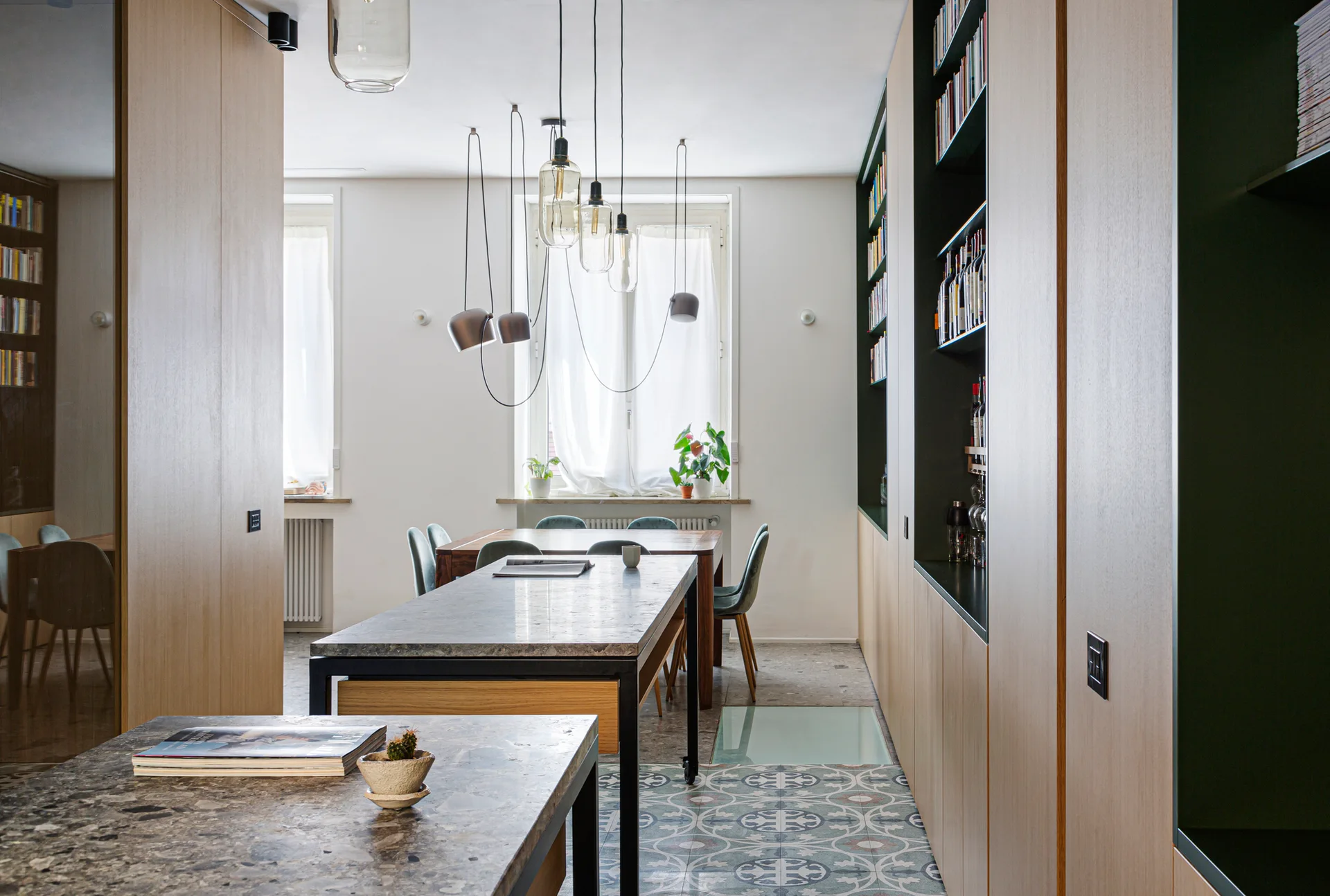 A dining room features full-height wood cabinetry with dark green recessed shelves, a stone-topped island, and a patterned tile floor.