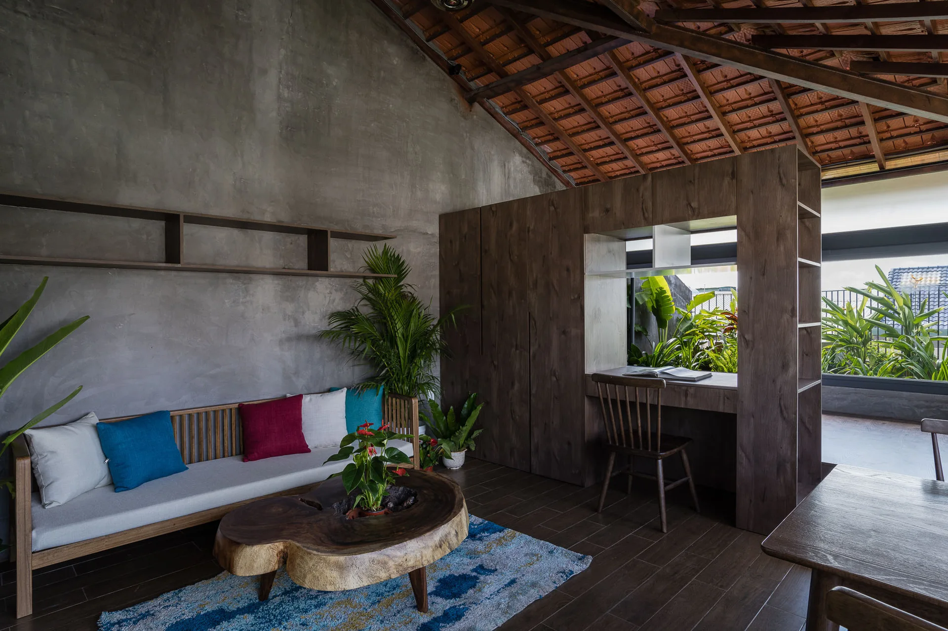 A living room with textured grey concrete walls, a vaulted wooden ceiling, a live-edge wood coffee table, and a built-in wooden desk unit.