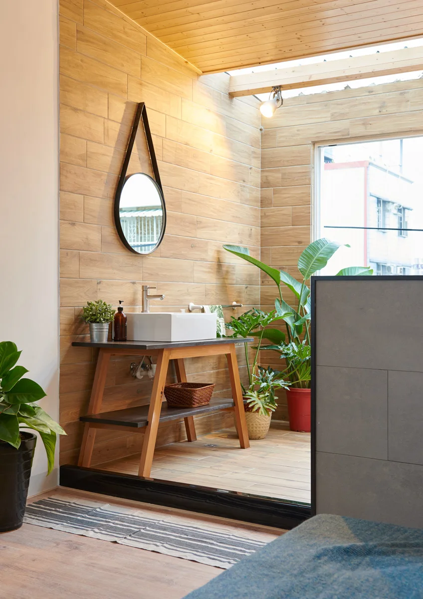 A wooden bathroom vanity with a white vessel sink sits against wood-look tiled walls under a bright skylight.