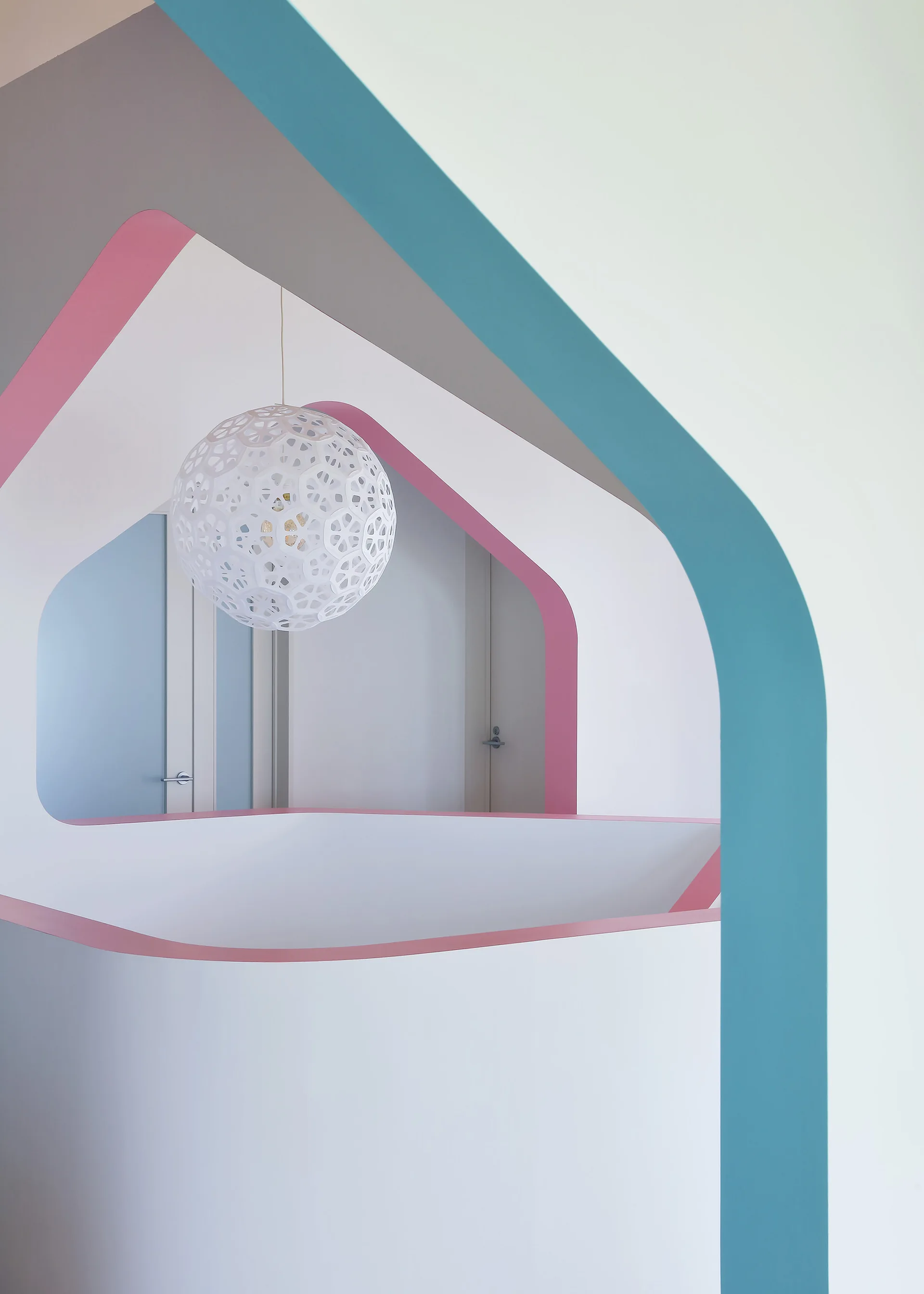 A modern hallway viewed through nested, colorful archways painted with teal and pink trim, featuring a white patterned spherical pendant light.