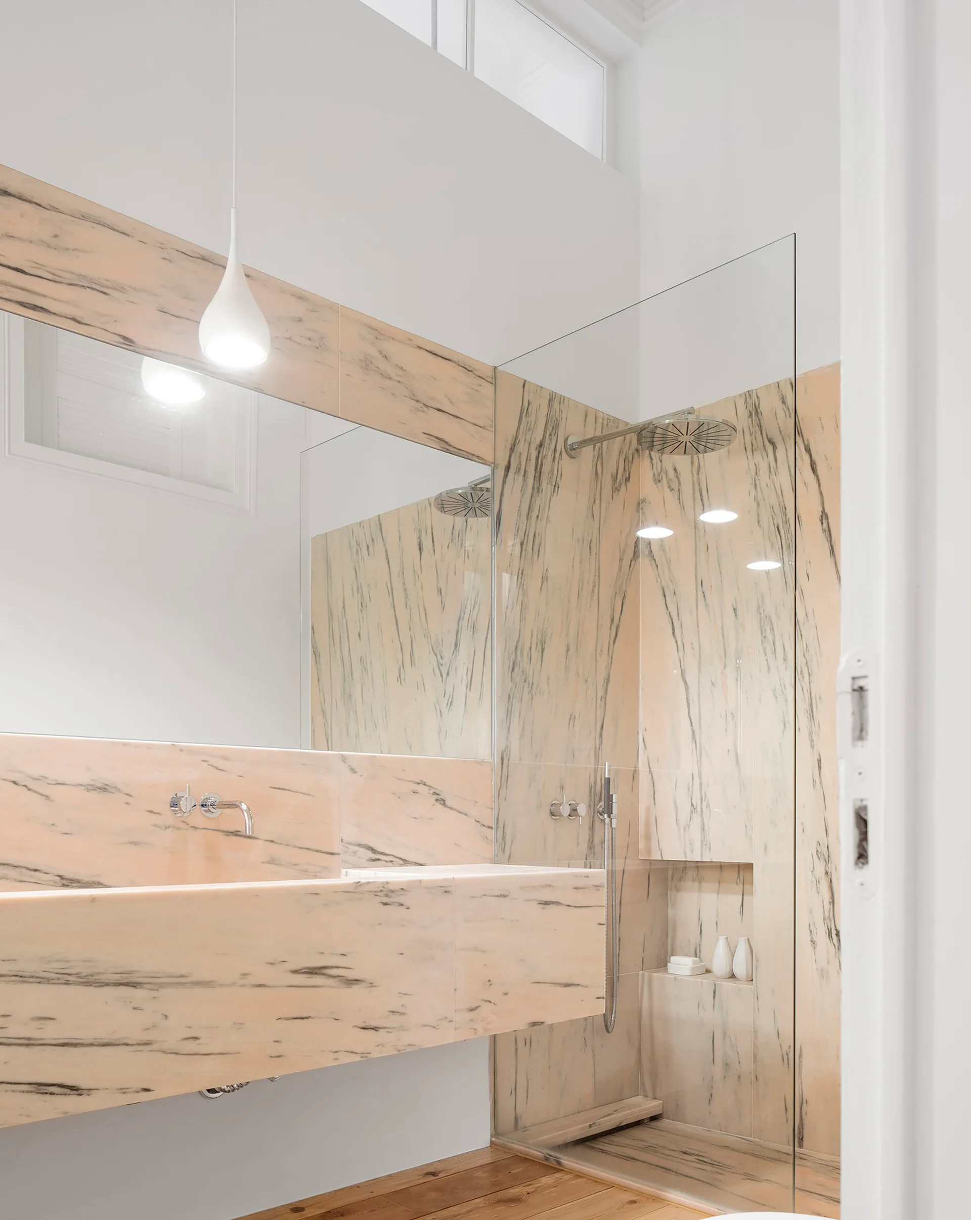 A minimalist bathroom with a peach veined marble wall-mounted vanity and a glass walk-in shower.