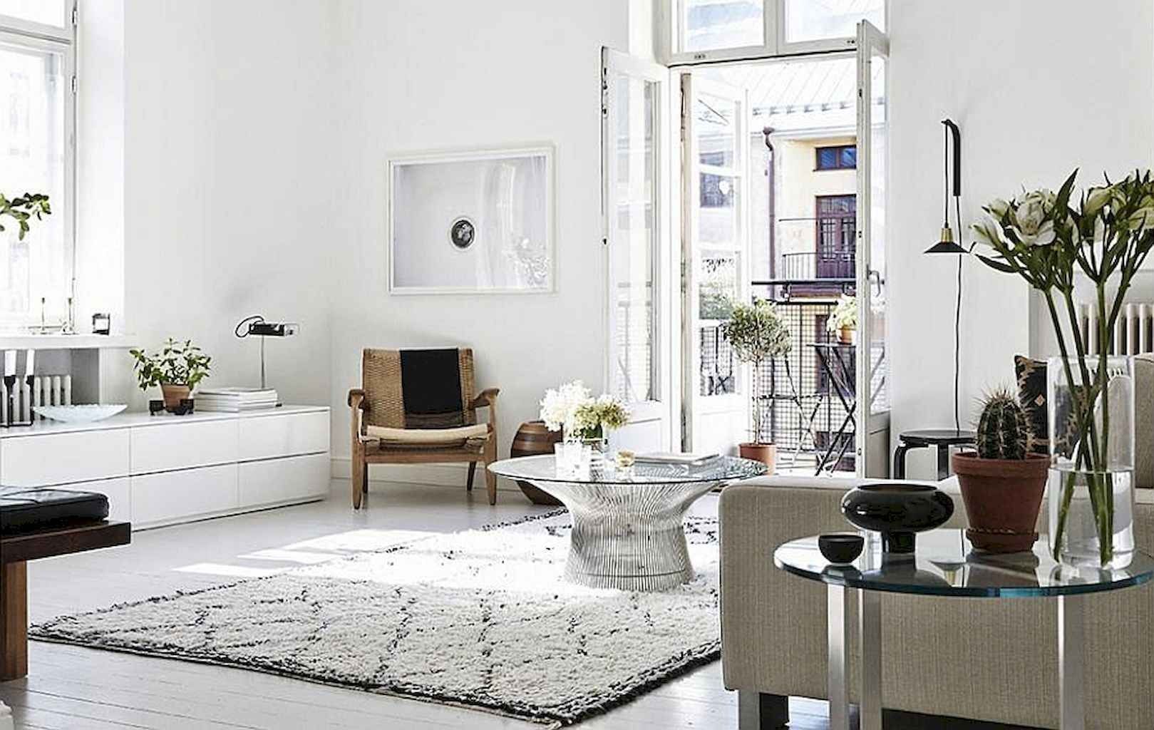 A bright white Scandinavian living room features a textured shag rug, glass coffee table, and an open balcony door letting in natural sunlight.