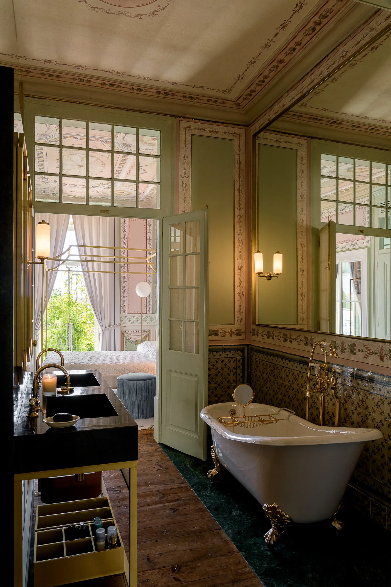 A vintage style bathroom features a white clawfoot bathtub and a black marble vanity with gold faucets next to a paneled door.