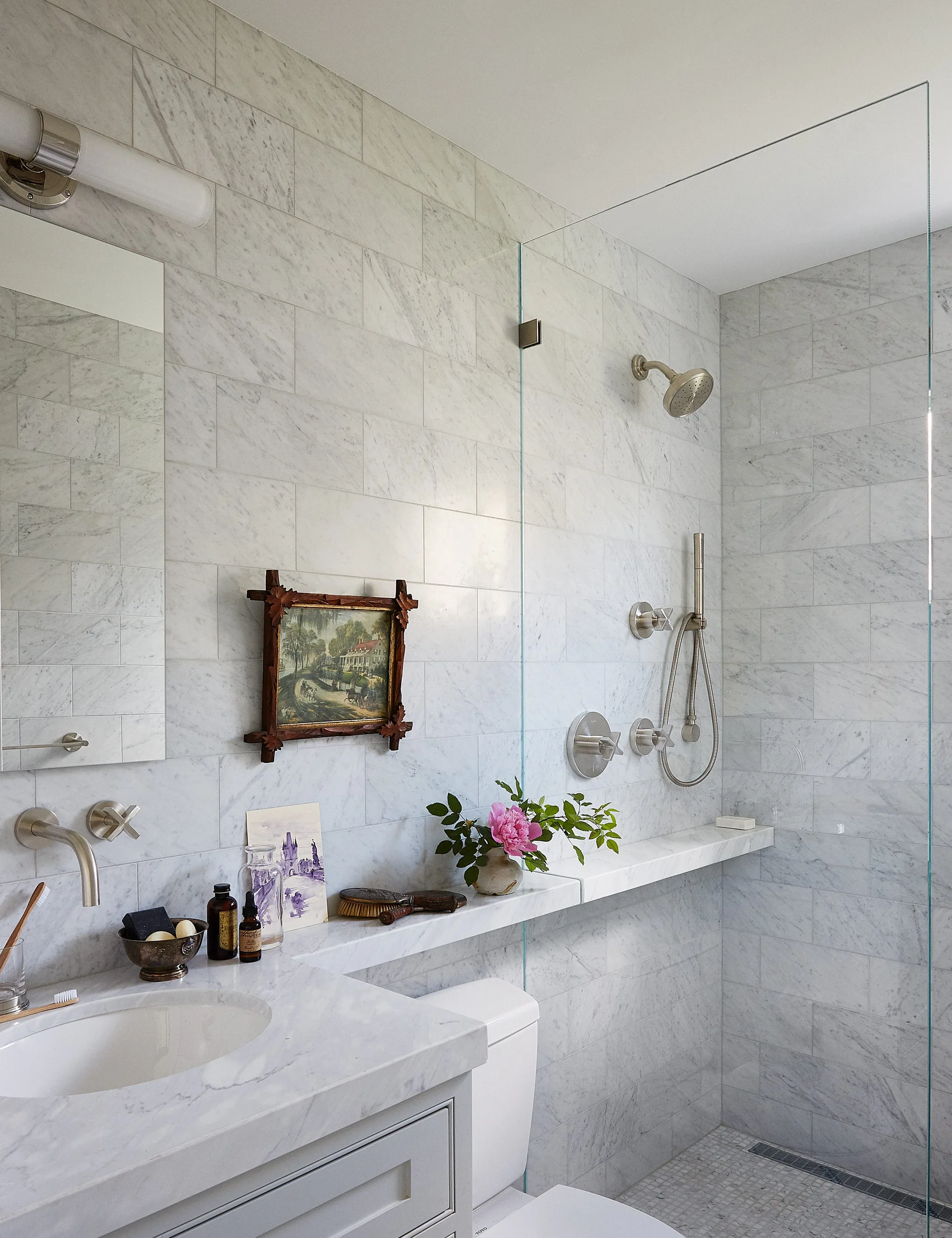 A marble-tiled bathroom with a glass shower enclosure, a vanity sink, and a continuous stone ledge running along the back wall.