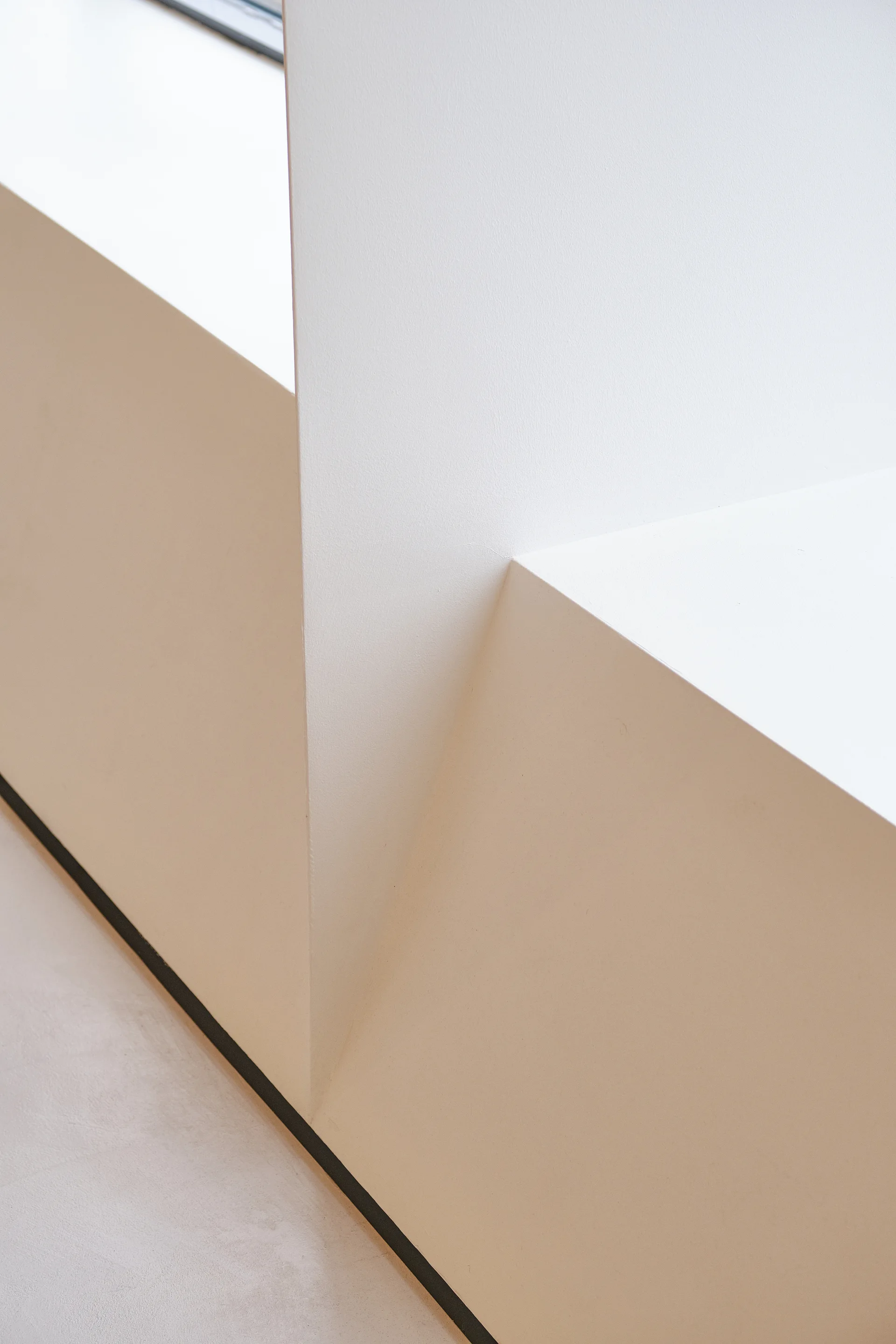 A close-up view of sharp geometric plaster walls intersecting with a built-in off-white bench ledge under soft, diffuse lighting.