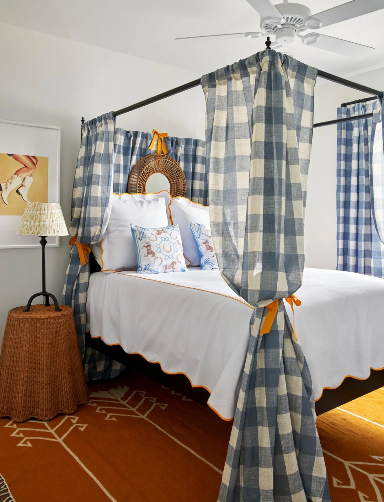 A bedroom features a black four-poster canopy bed dressed in blue and white gingham curtains and white bedding with orange scalloped trim.