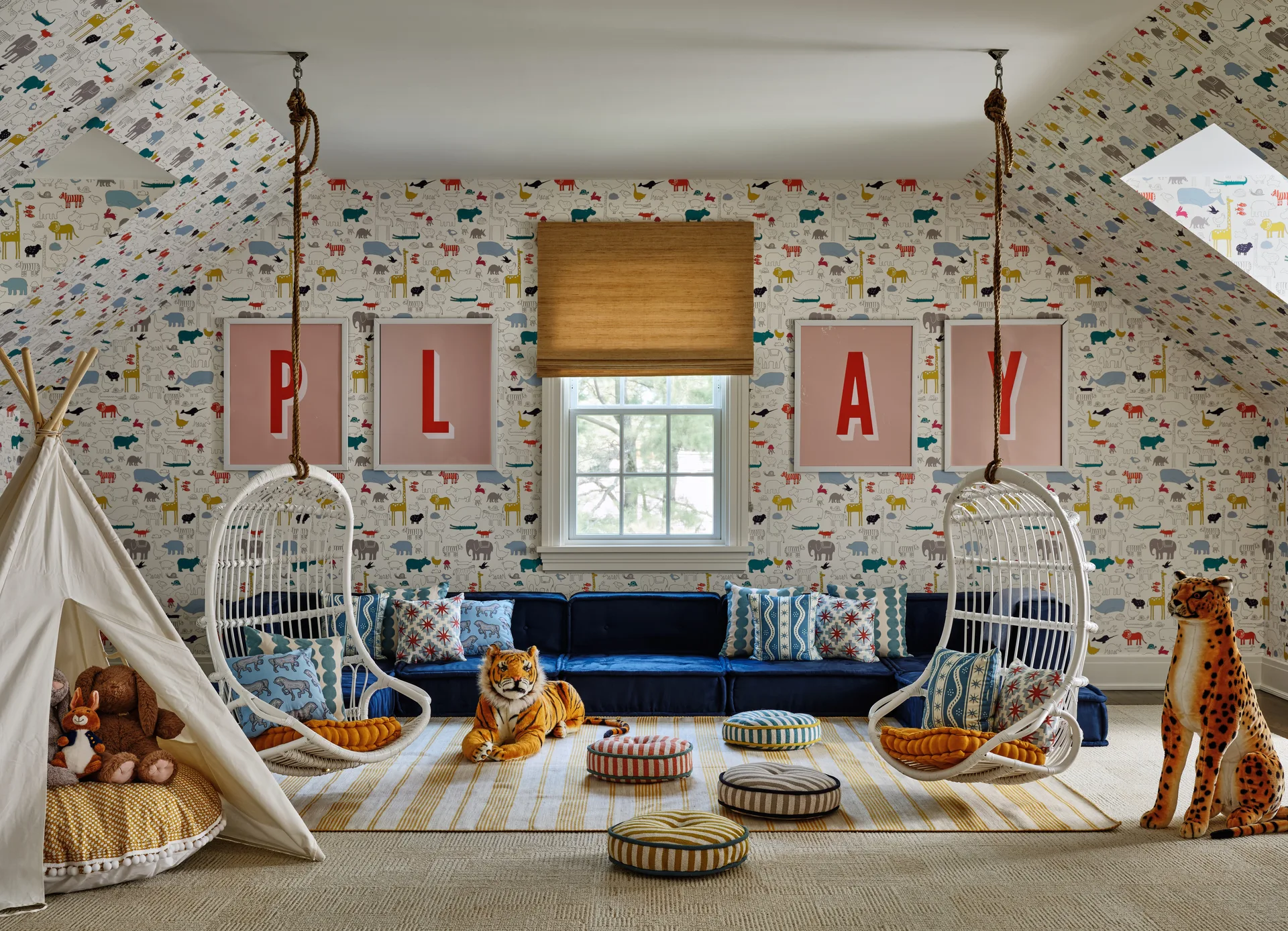 A playful attic playroom featuring two suspended white rattan egg chairs, a low navy blue velvet sofa, and whimsical animal-patterned wallpaper.