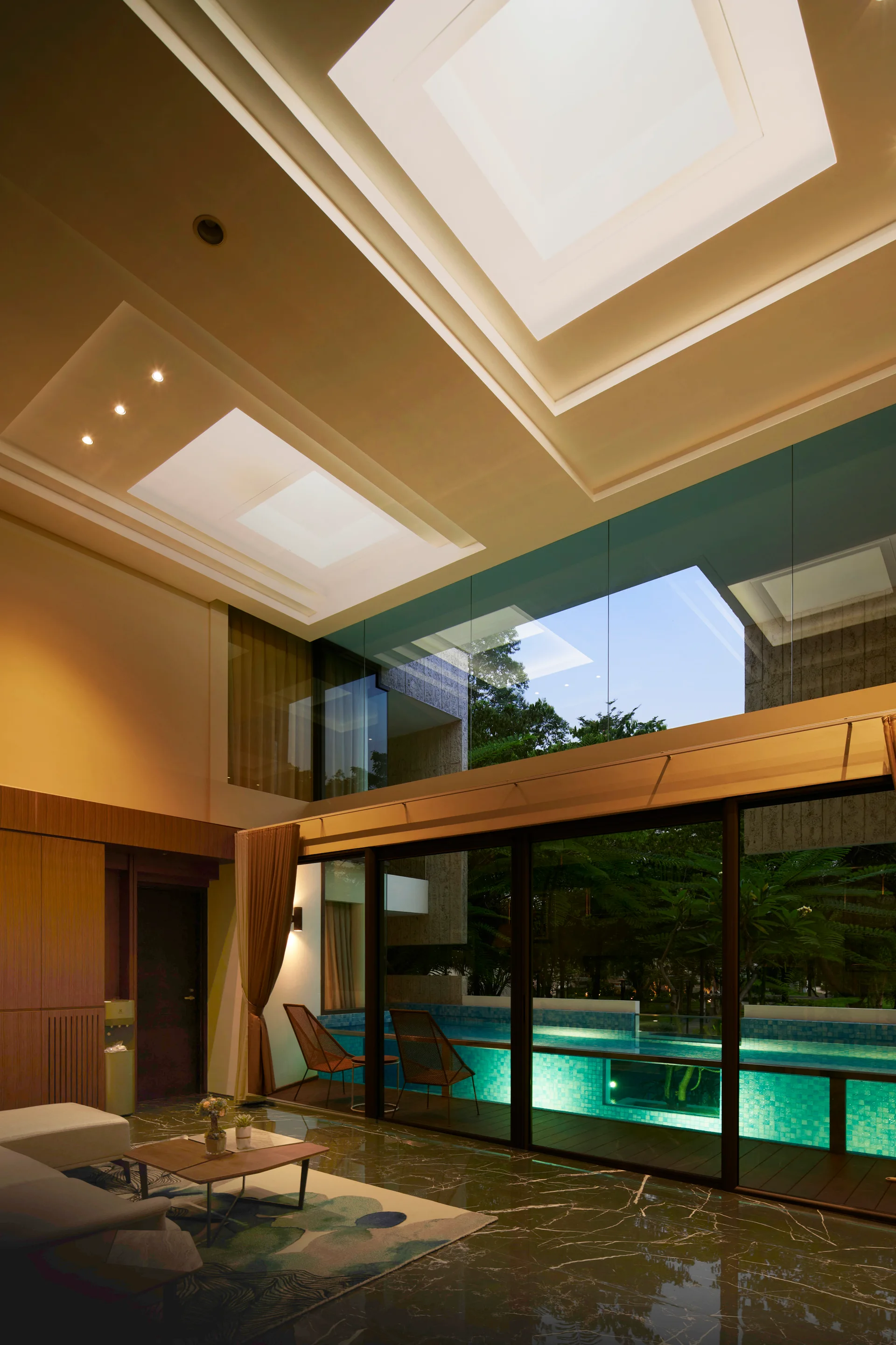 A contemporary living room features dark polished marble floors, a patterned rug, and a large glass wall looking out to an illuminated swimming pool.