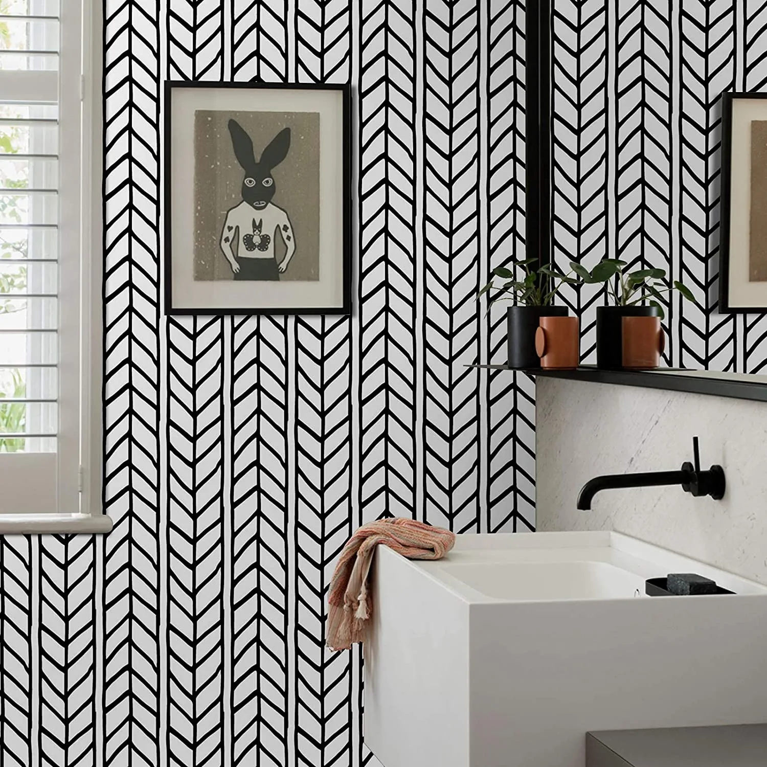 A bathroom vanity features black and white herringbone wallpaper, a white rectangular sink with a matte black faucet, and a framed rabbit artwork.