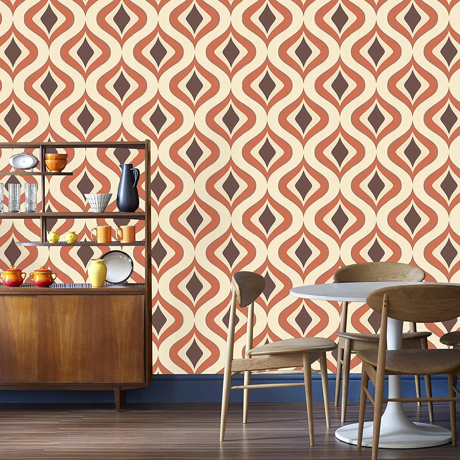 A mid-century dining room features retro orange geometric wallpaper behind a wooden shelving unit and a white circular table with chairs.