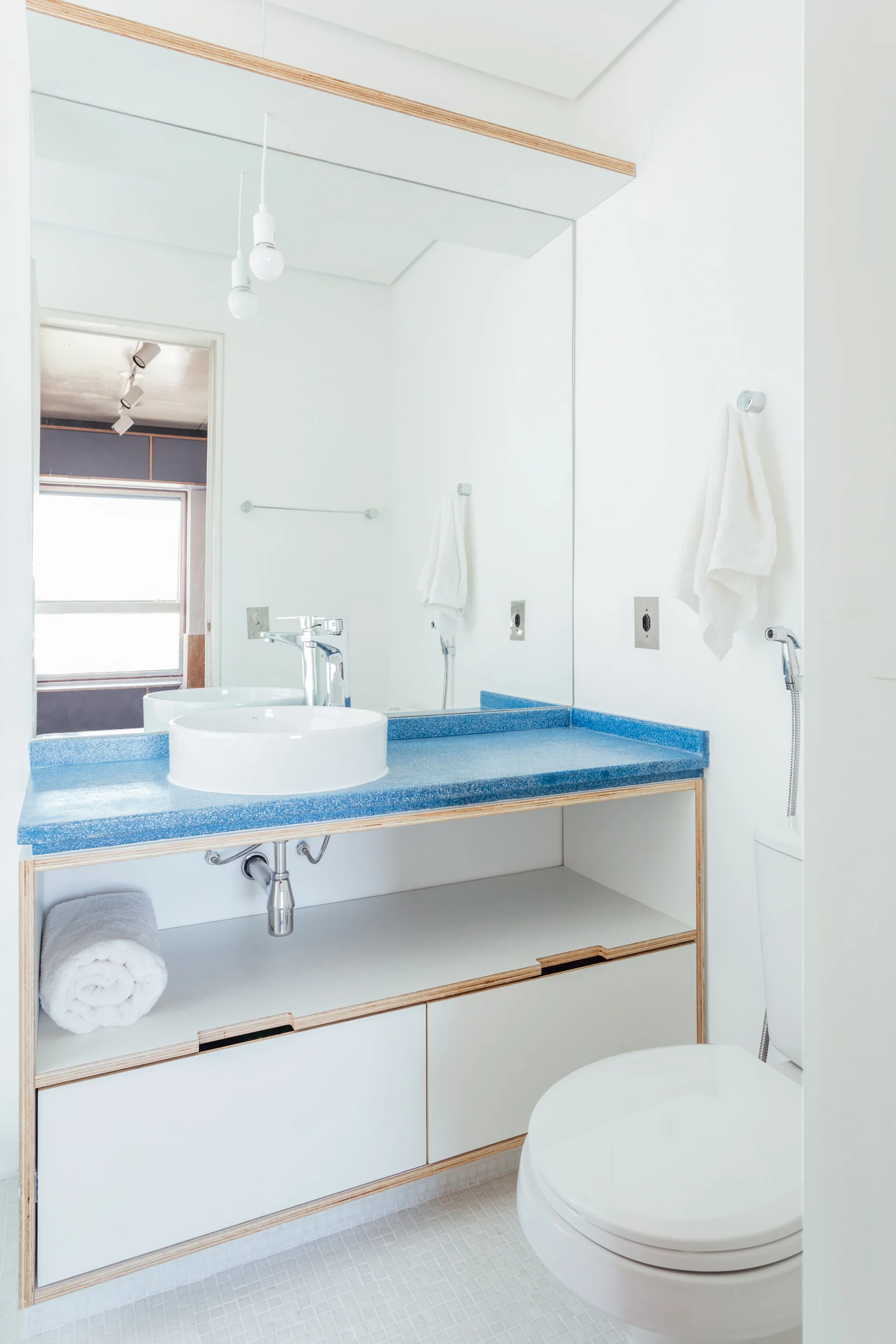 A modern bathroom features a white vessel sink on a bright blue countertop with a plywood-edged vanity and a matching large mirror.