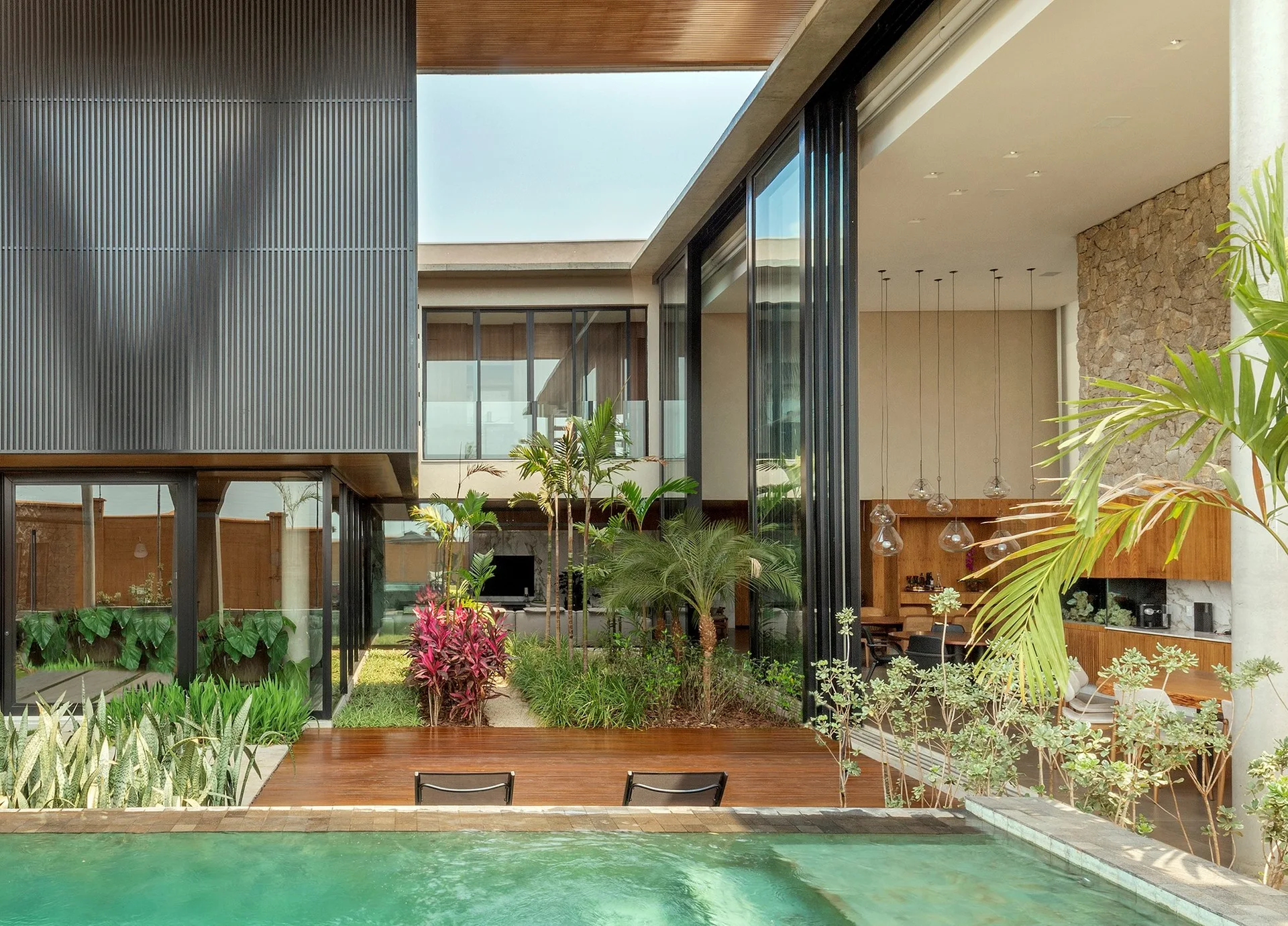 A modern home with an open courtyard garden, a swimming pool in the foreground, a wooden deck, and sliding glass doors opening to the interior.