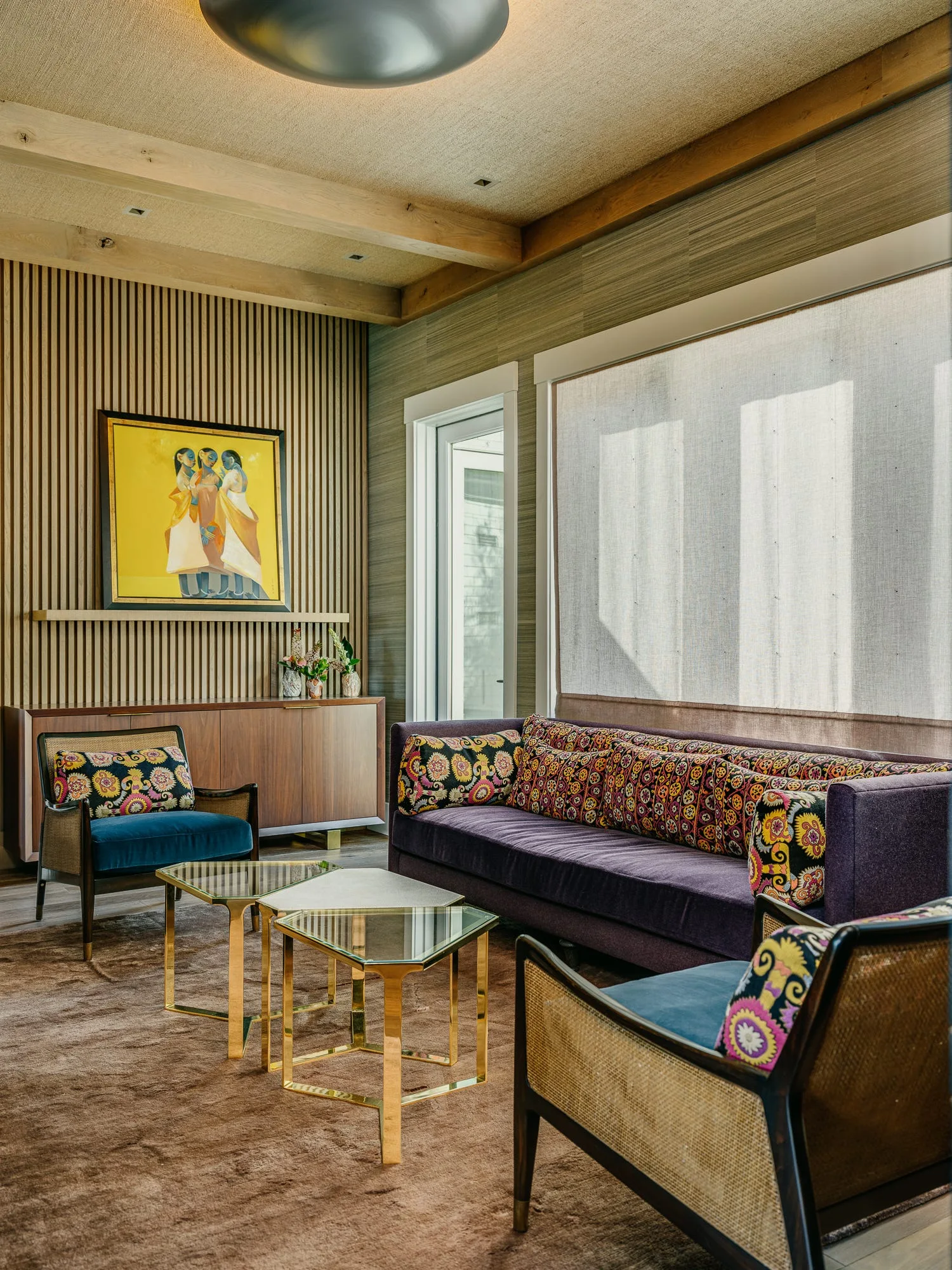 A living room features a purple velvet sofa, two blue cane-back chairs, geometric gold coffee tables, and a vertical wood slat accent wall.