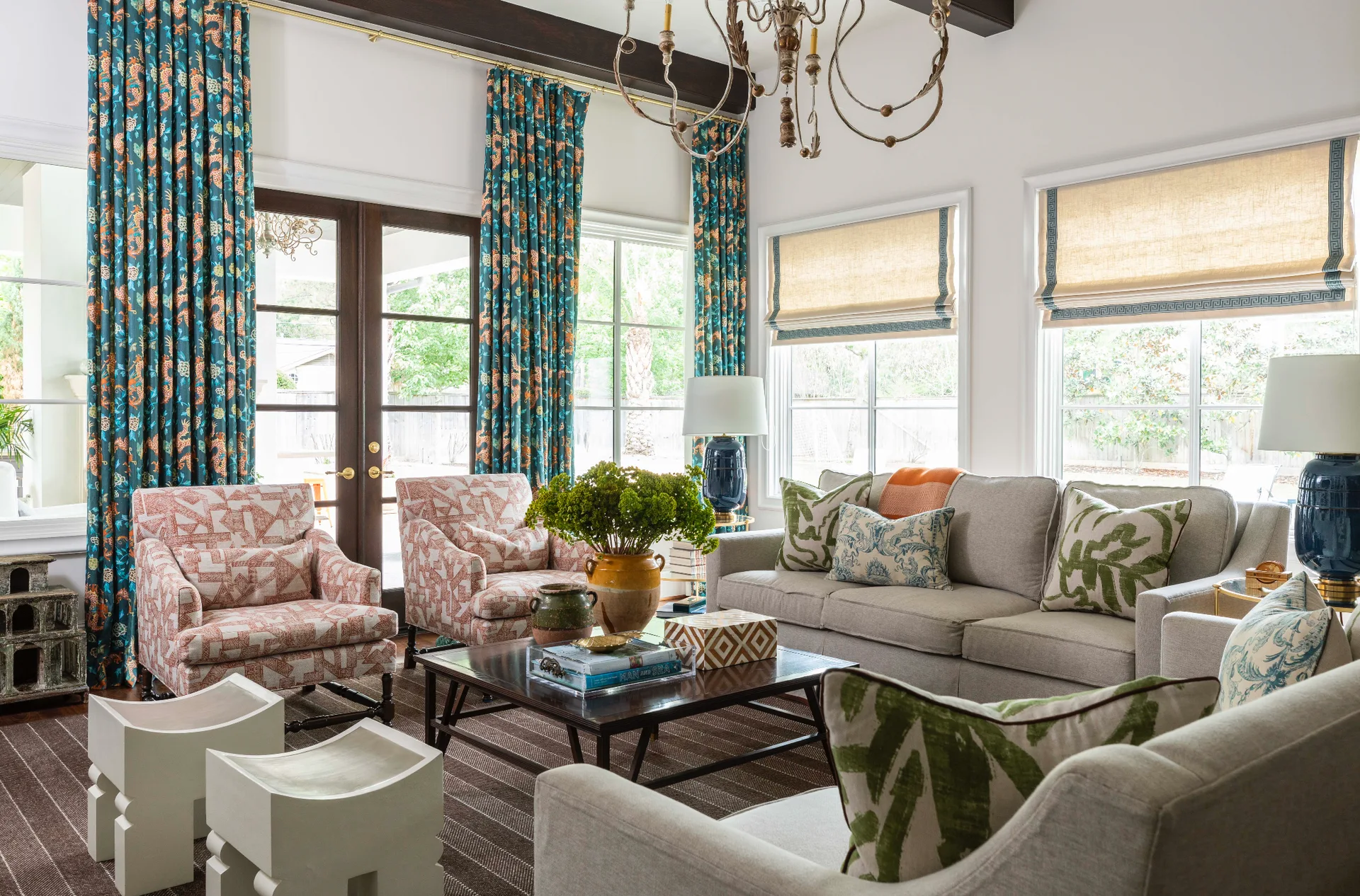 A living room features a grey sofa, patterned teal curtains, two orange patterned armchairs, and dark wood ceiling beams.