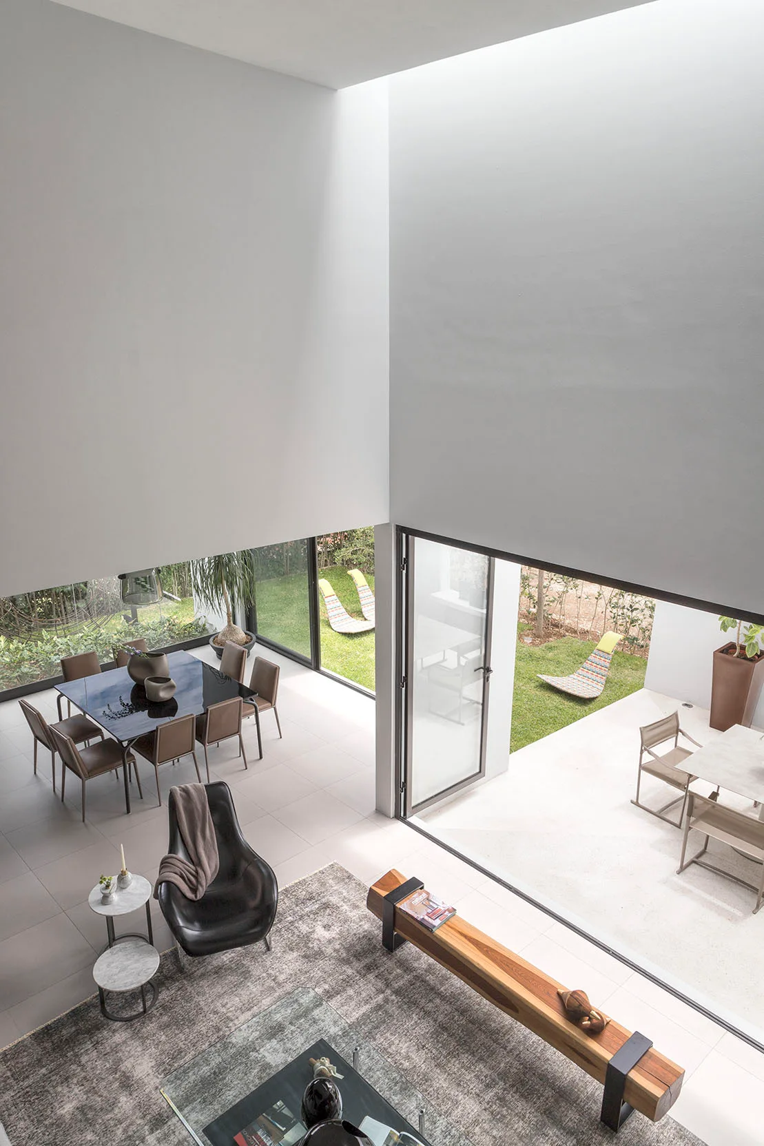 High-angle view of an open living and dining space with a solid wood bench, a dining table, and sliding glass doors opening to a yard.