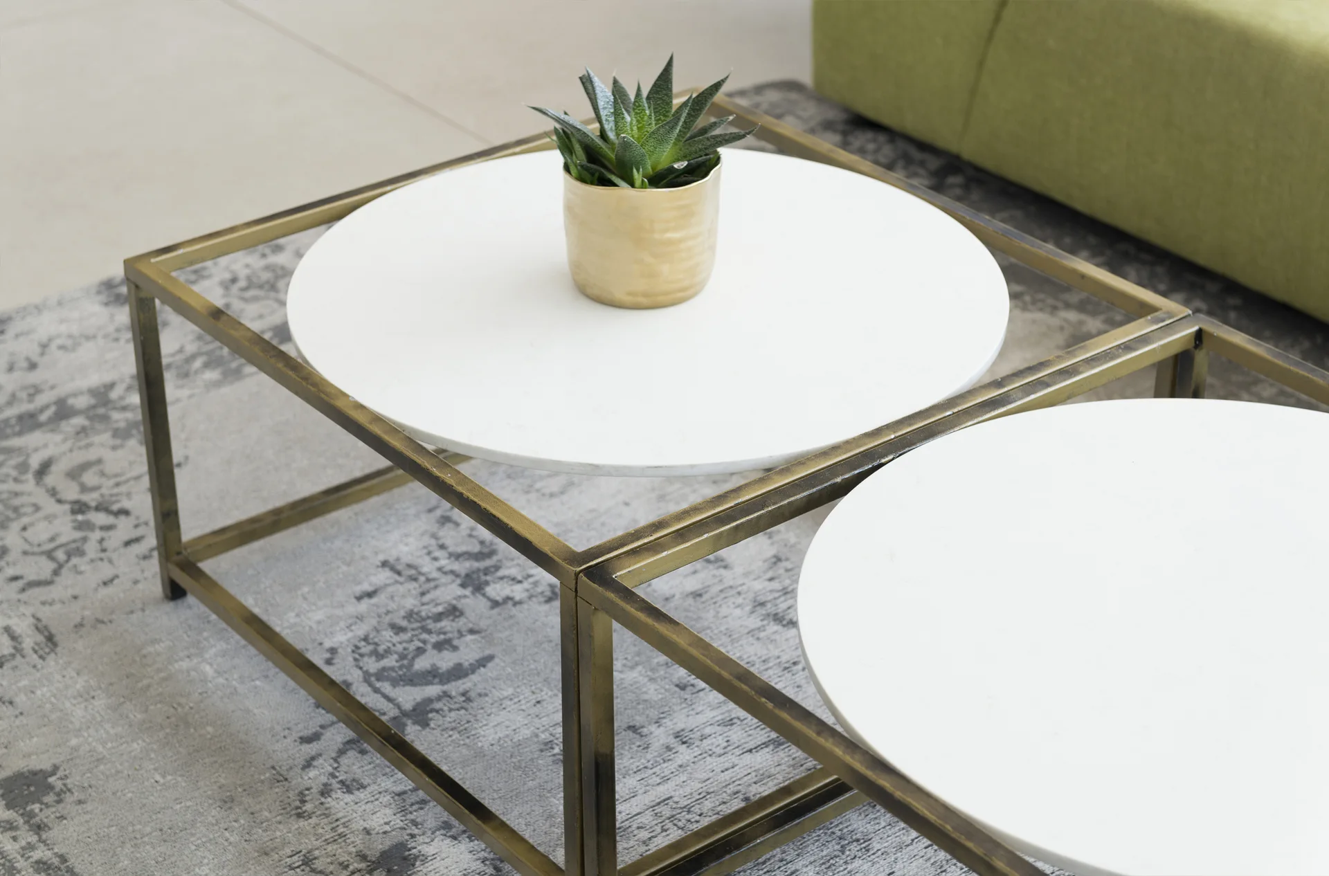 Two square brass-framed nesting coffee tables with circular white tops sit on a distressed grey patterned rug.