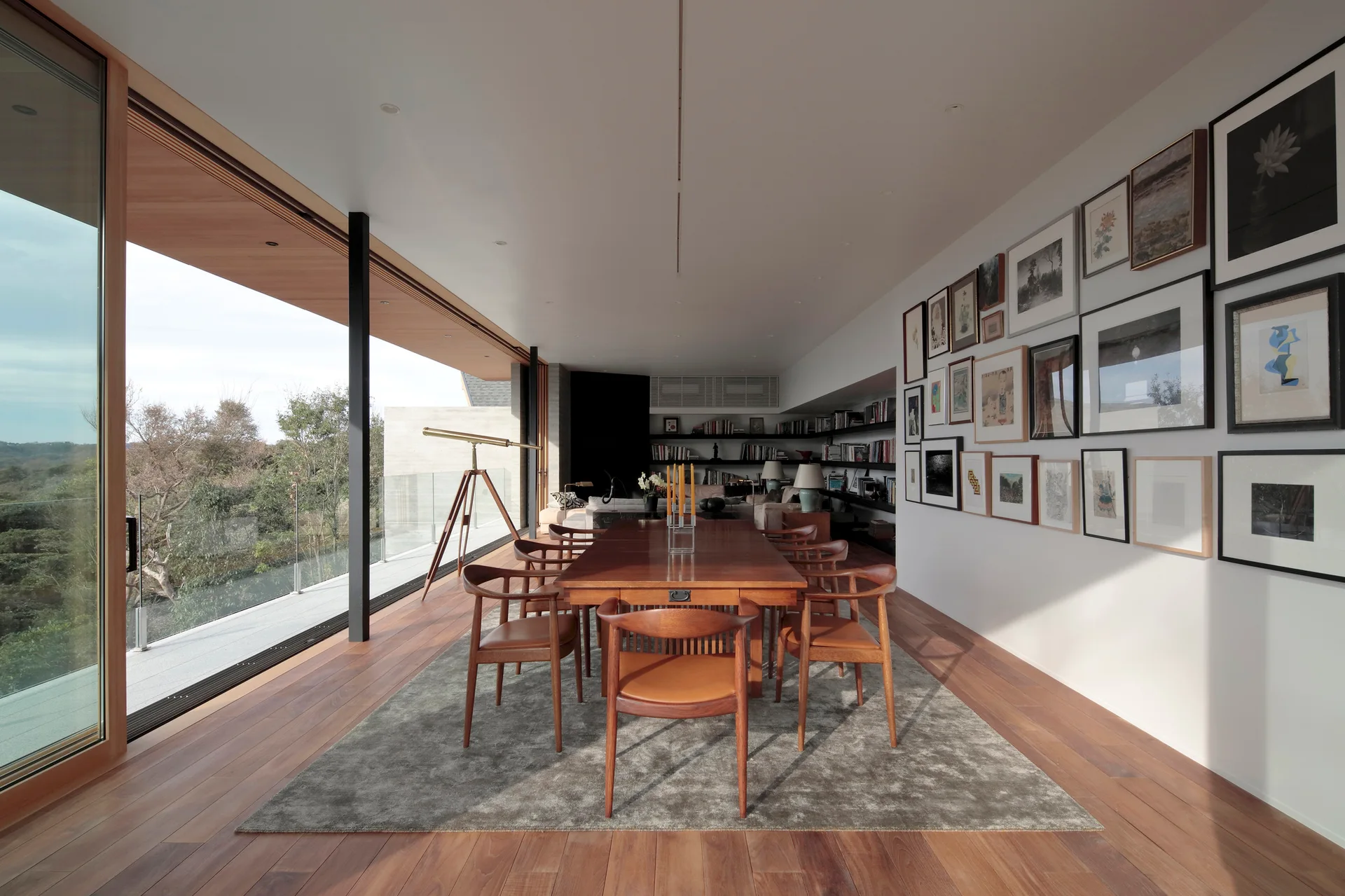 A mid-century wood dining table and chairs sit on a grey rug next to a dense wall-mounted gallery art display.
