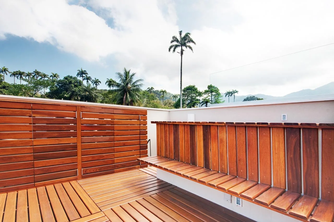 A modern outdoor terrace features a slatted wood deck, a matching built-in wooden bench, a tall wood privacy screen, and a clear glass railing.