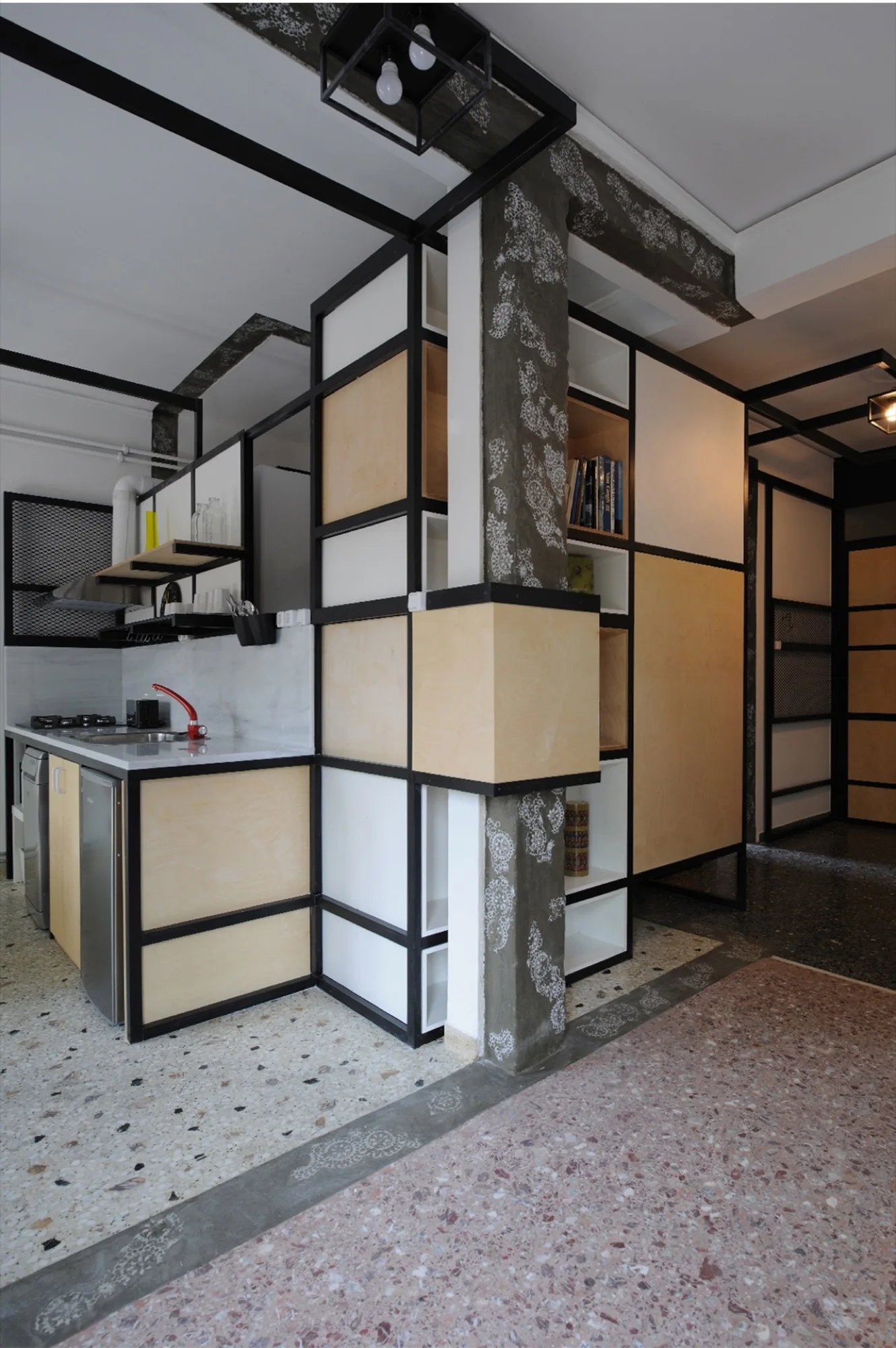 A modern industrial kitchen with light plywood cabinets in black metal frames, a terrazzo floor, and an integrated structural column.