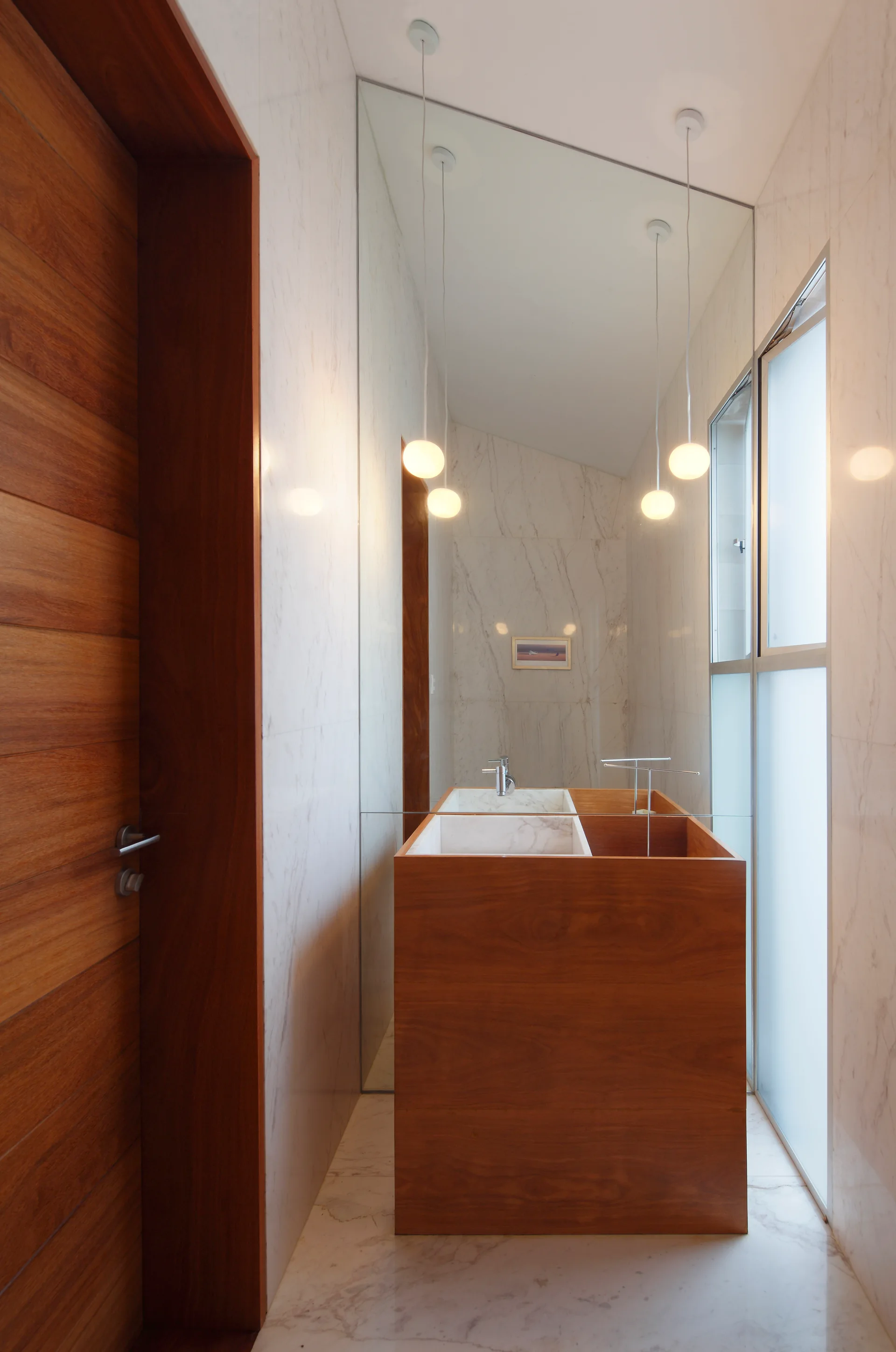 A modern bathroom featuring a freestanding wood vanity with a marble sink, a tall mirror, and white marble walls.