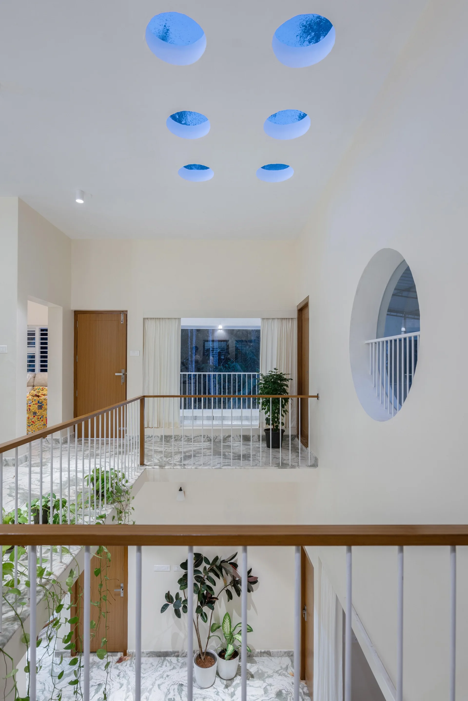 A multi-level staircase landing features circular skylights in a white ceiling, polished marble flooring, and white railings with wooden handrails.