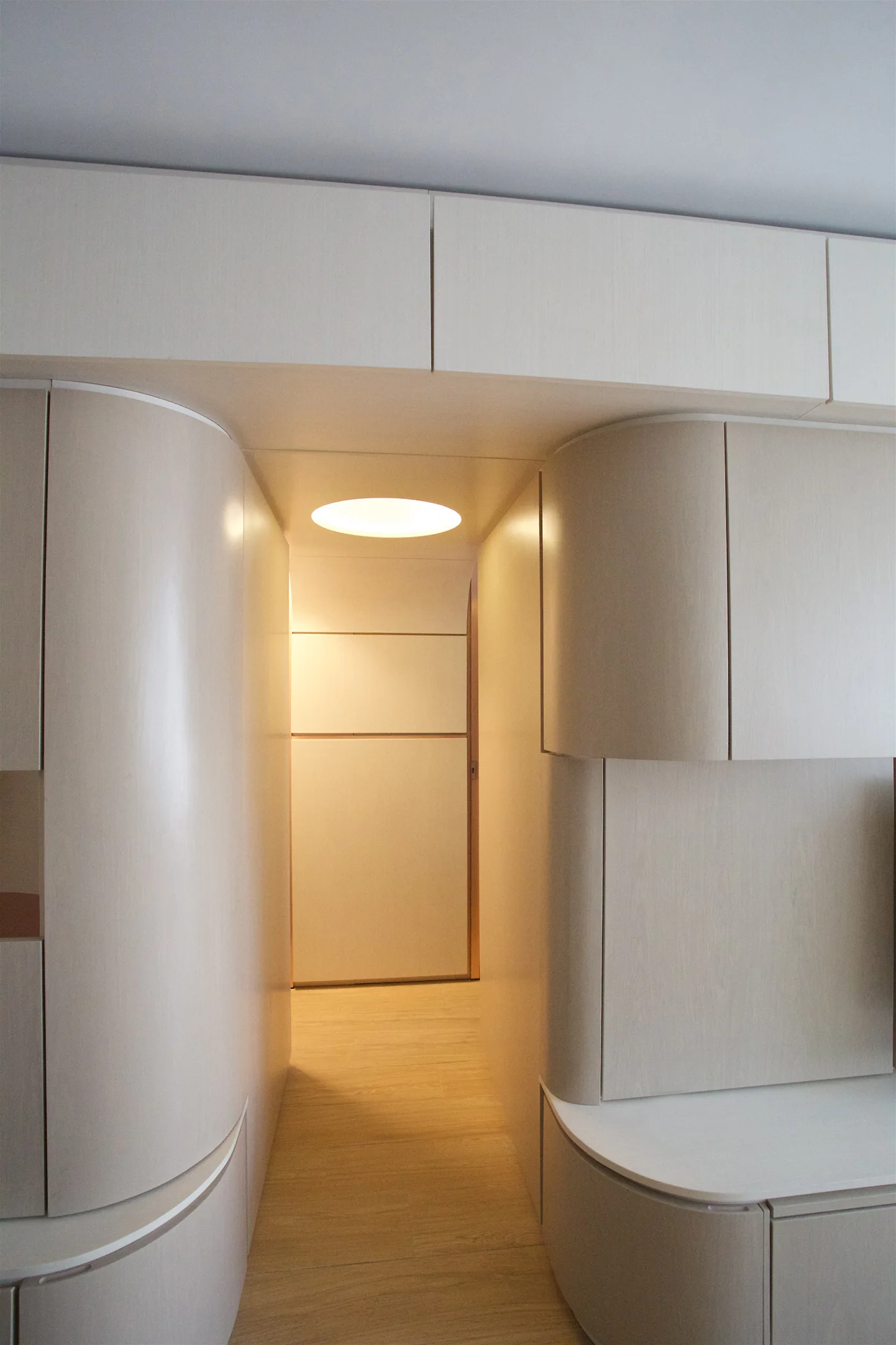 A minimalist hallway framed by custom cream cabinetry with rounded corners and a warm circular recessed ceiling light.