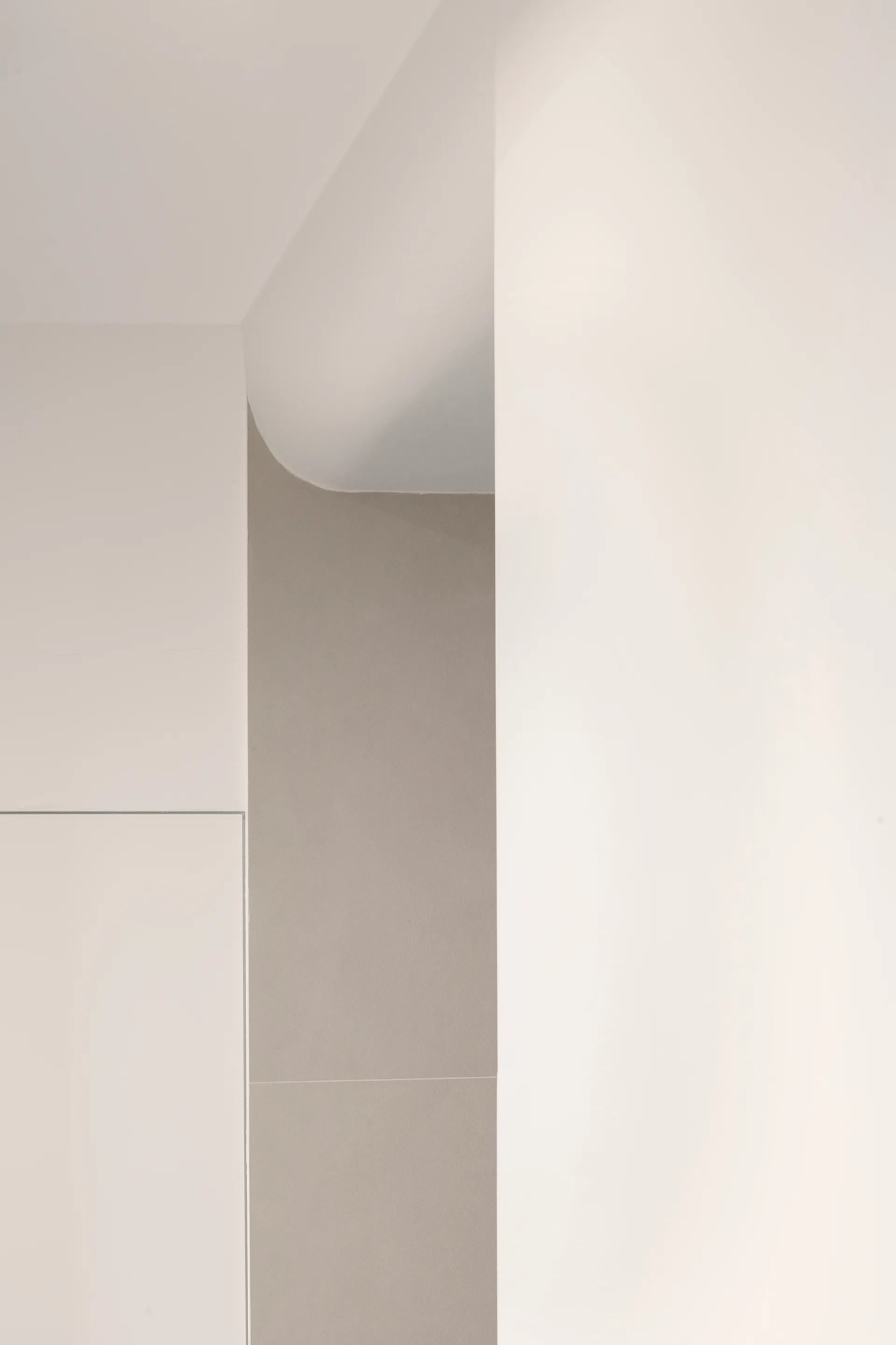 Minimalist interior wall intersection featuring a curved white ceiling soffit next to a recessed light grey panel.