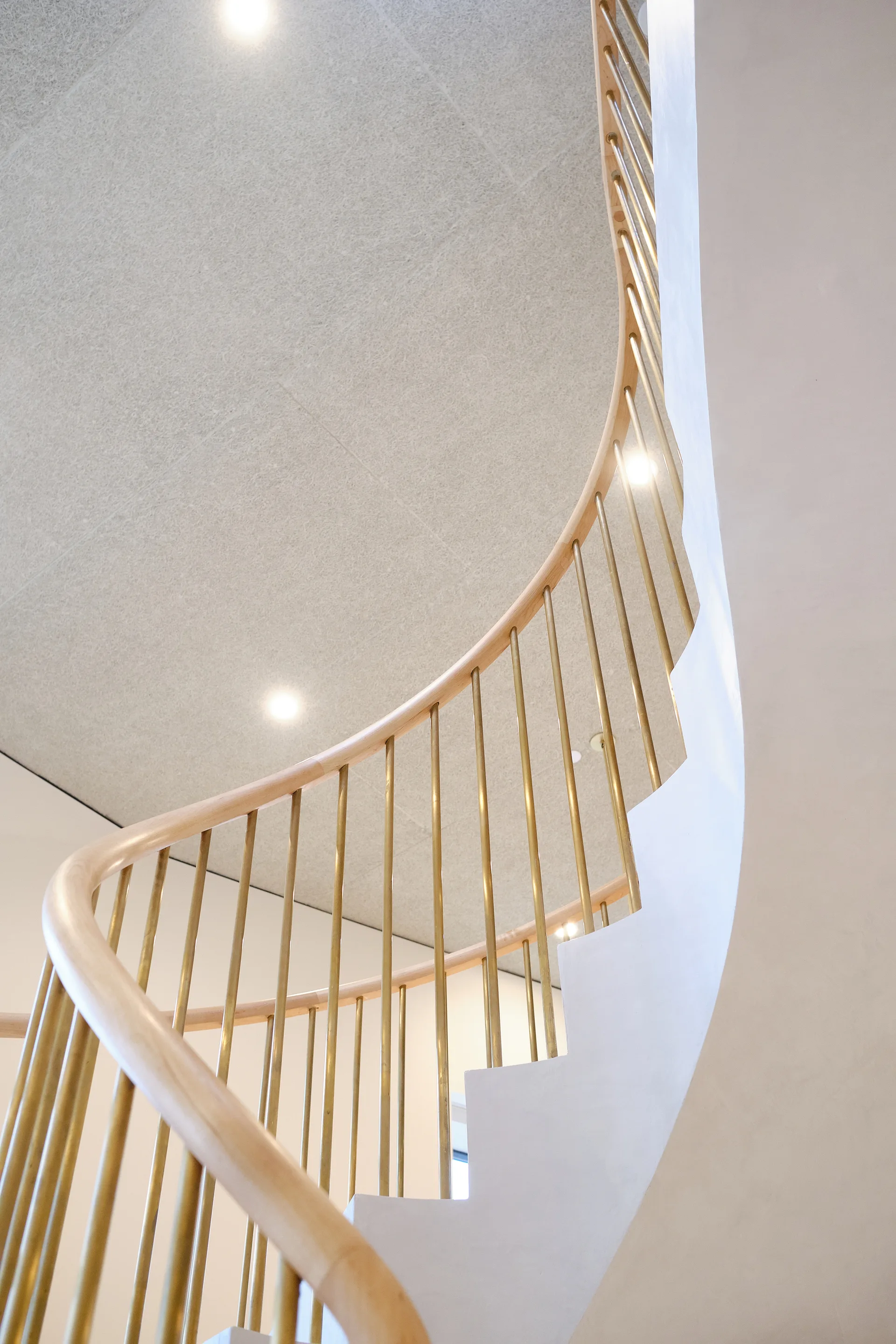 A curved off-white staircase features vertical brass spindles and a light wood handrail sweeping upward toward a textured ceiling.