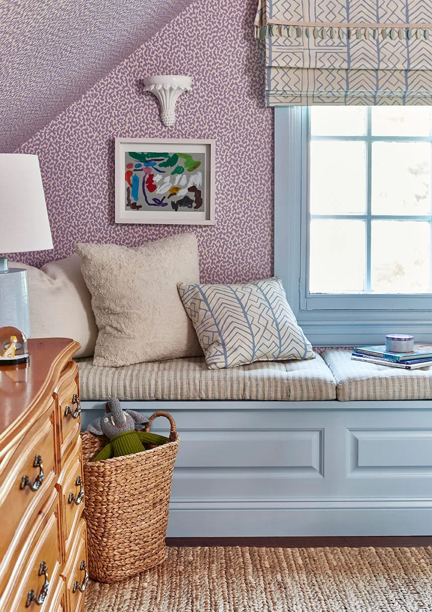 A built-in blue window seat with striped cushions sits against purple patterned wallpaper in an attic bedroom corner under a sloped ceiling.