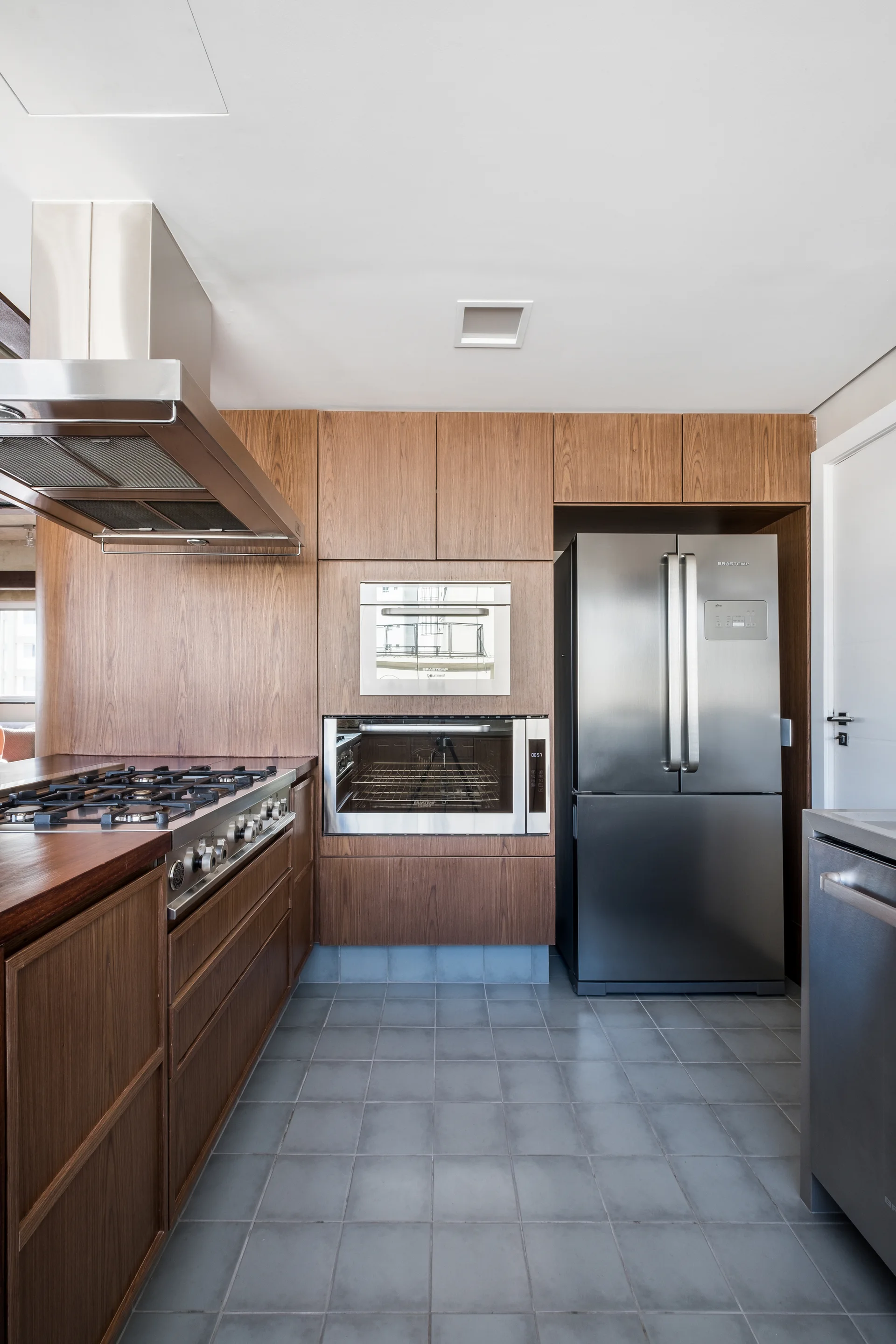 A modern kitchen featuring warm wood-toned flat-panel cabinetry, built-in stainless steel appliances, and grey tiled flooring.