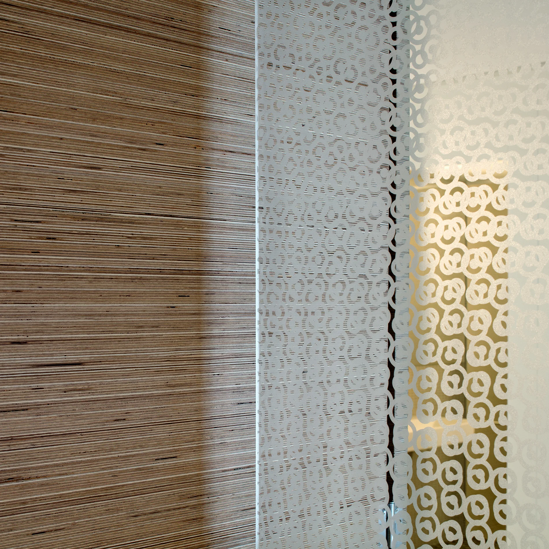 A close-up view of a horizontally layered wood wall next to a frosted glass partition etched with a repeating circular pattern.