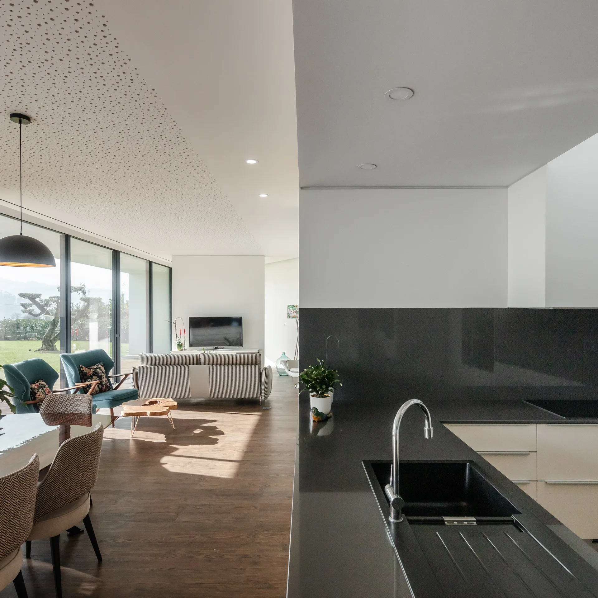 A modern open-concept kitchen features a dark gray island looking out toward a dining table and a living room with floor-to-ceiling windows.
