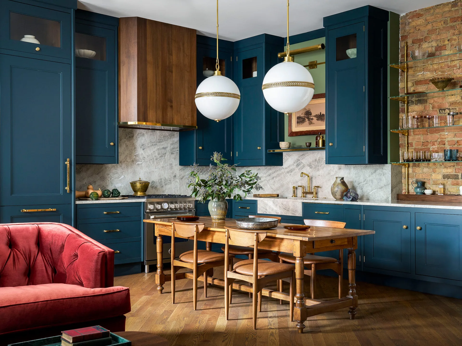 A kitchen with deep blue cabinetry, a marble backsplash, two spherical white pendant lights, and a central wooden dining table.