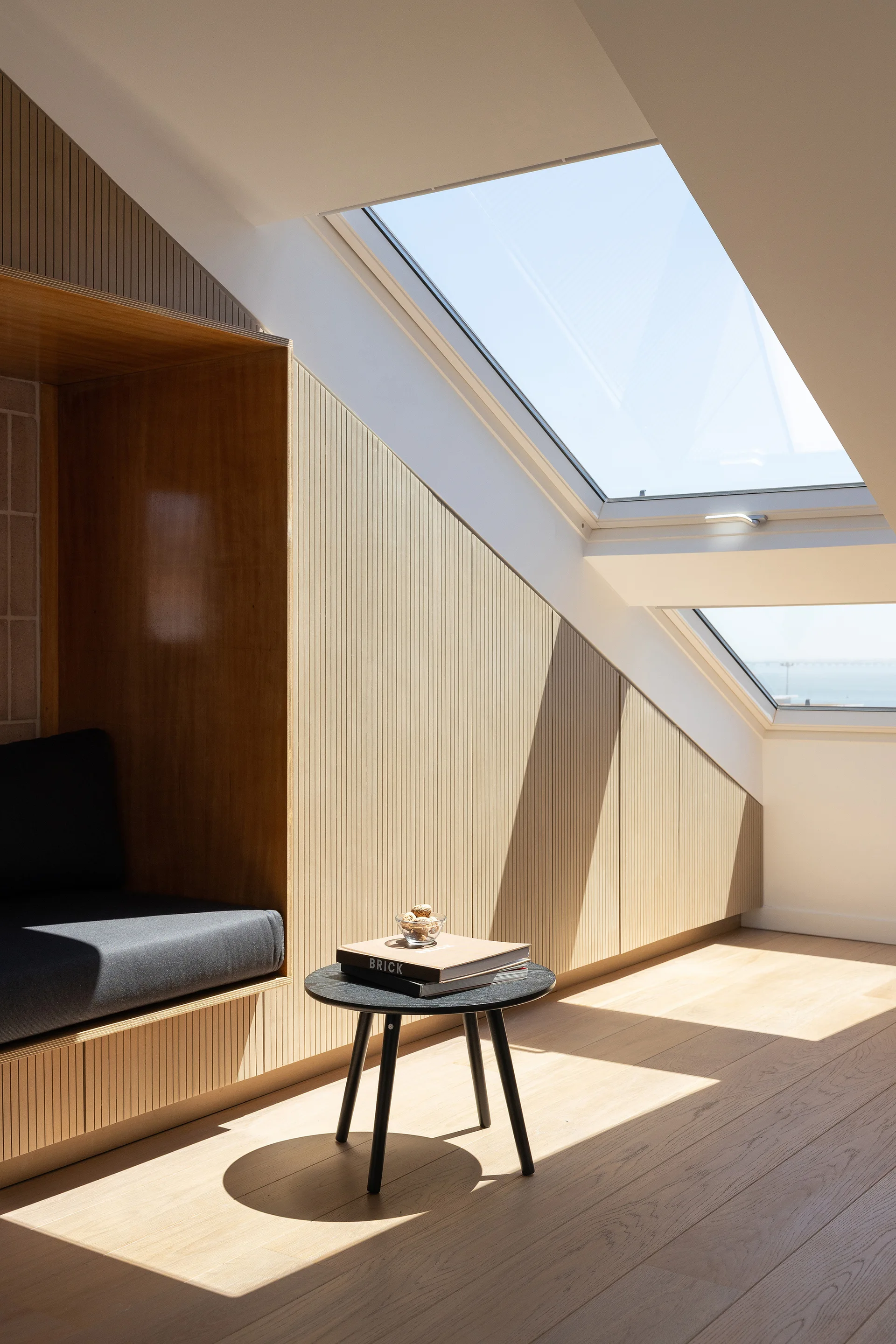 A sunlit attic room features a built-in wooden seating nook, vertical slatted wall paneling, and an angled skylight.