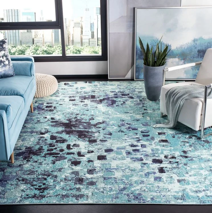 A modern living room features a blue sofa, a white metal-frame armchair, and a large blue abstract patterned rug in front of a city view window.