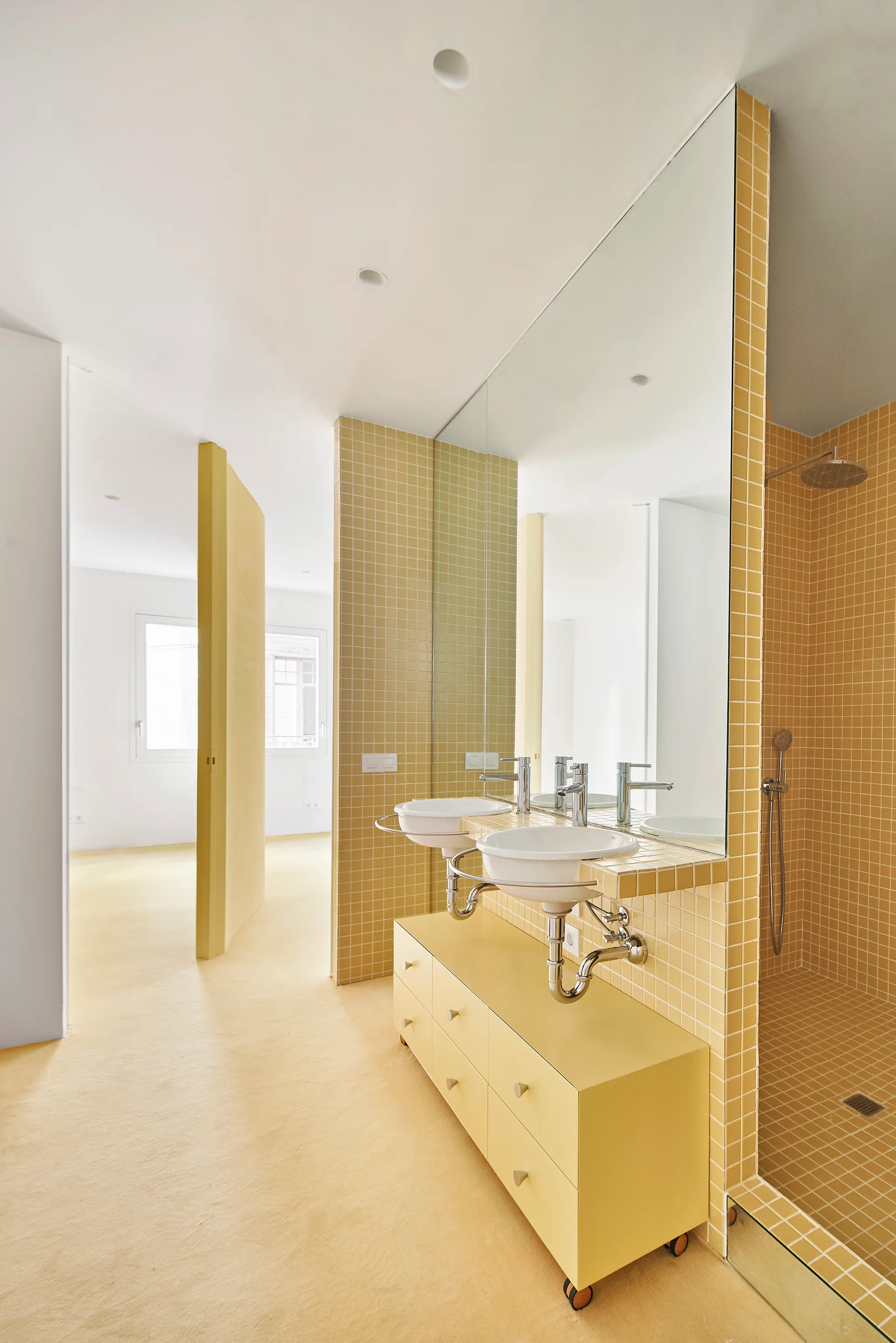A modern bathroom featuring yellow grid tiled walls, two white basin sinks, a large mirror, and a matching yellow cabinet on wheels.