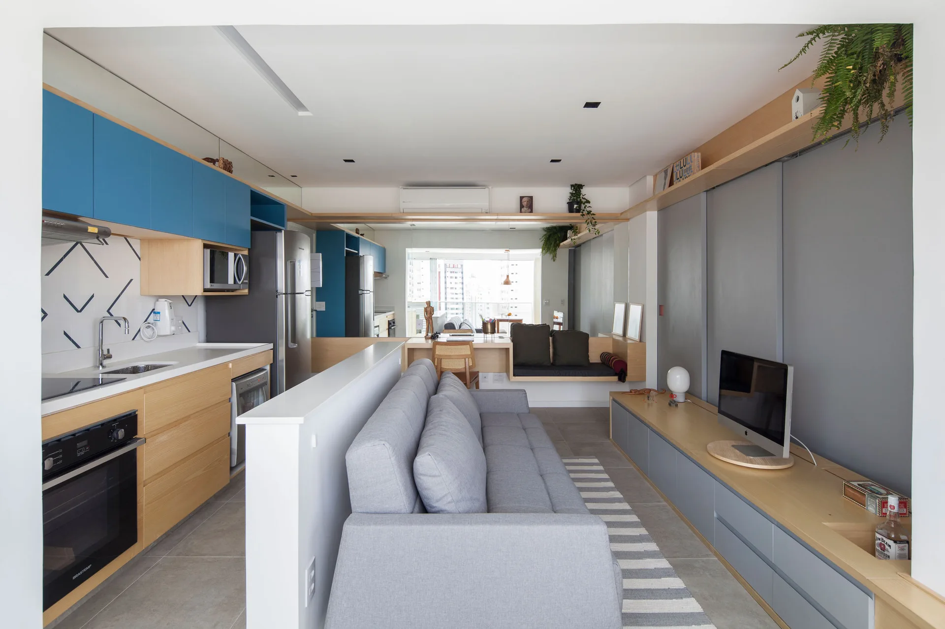 A small open-plan apartment features a grey sofa set against a low white divider wall next to a kitchen with blue upper cabinetry.