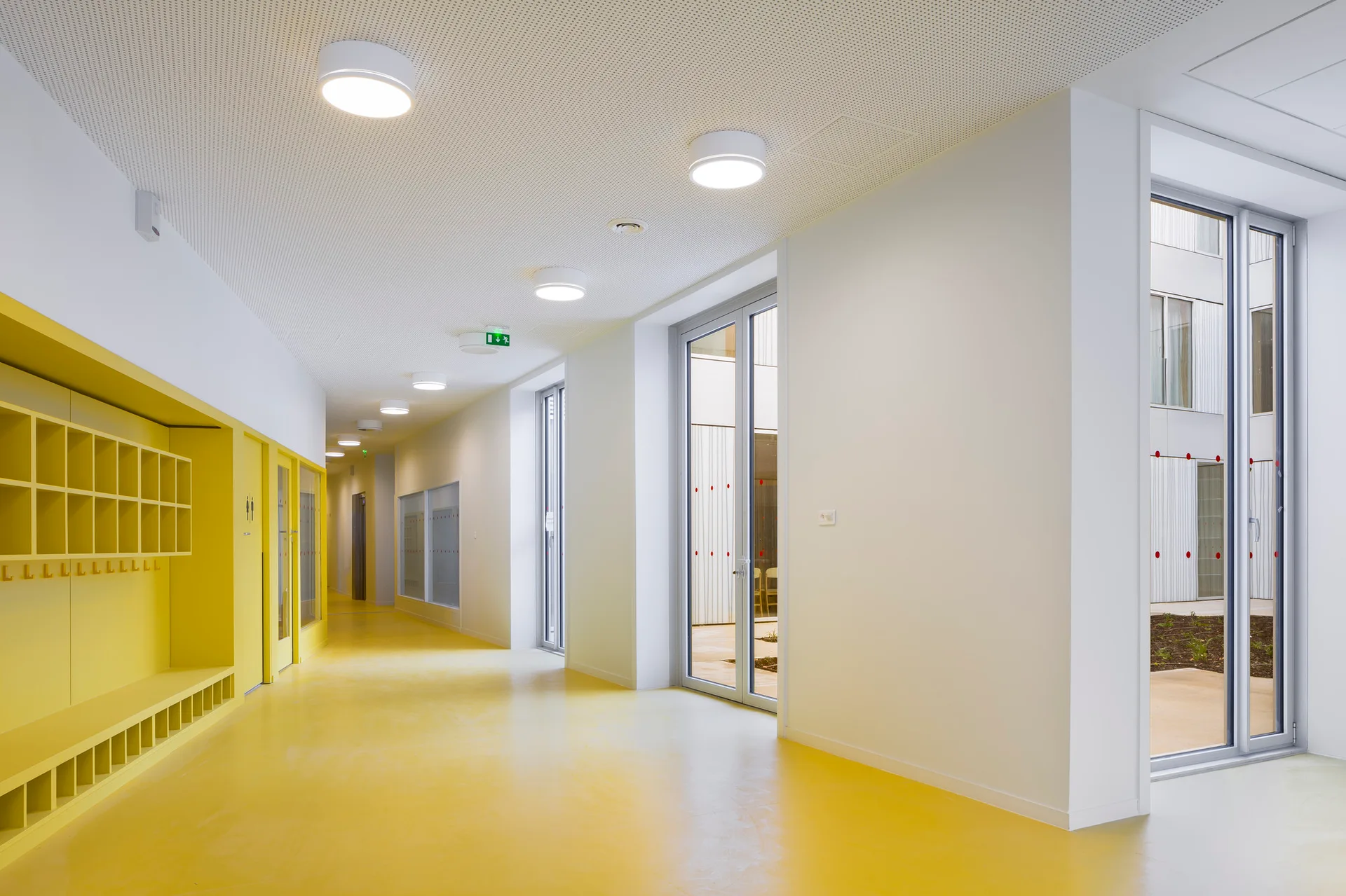 A long white hallway features a vibrant yellow floor, matching built-in yellow cubby storage, and glass patio doors.