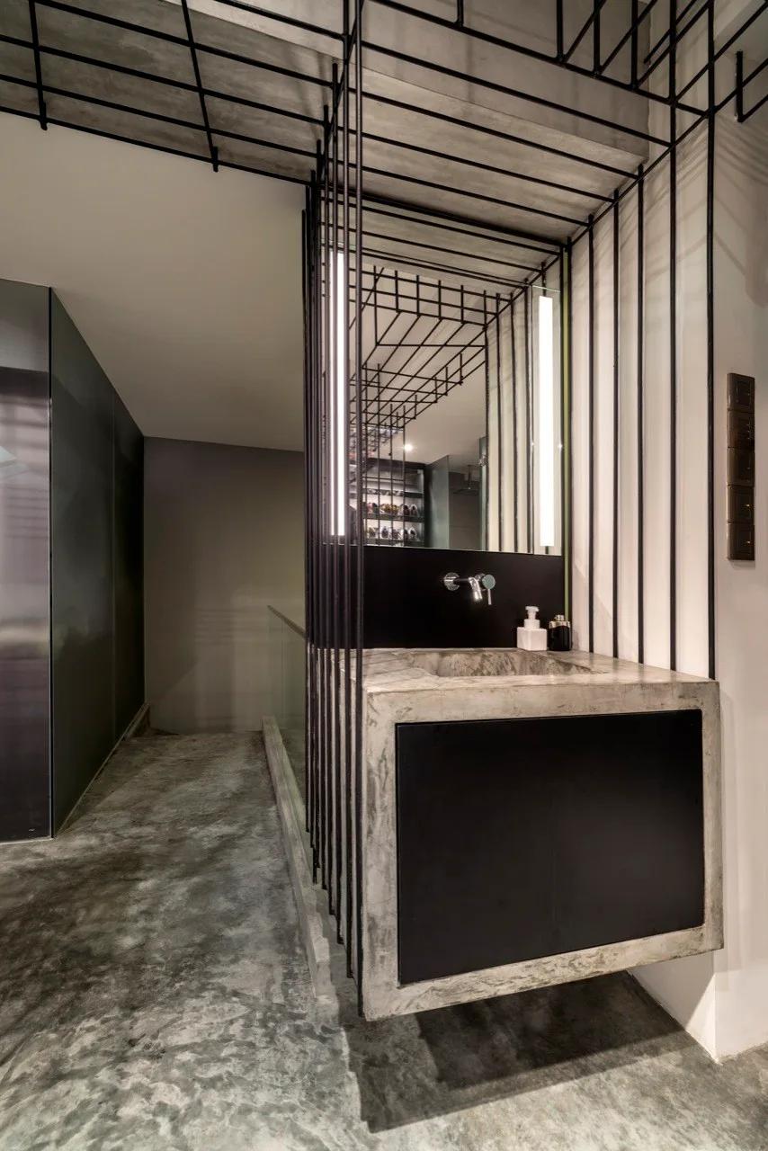 A minimalist floating concrete vanity with a black panel is enclosed by a black metal grid structure in an industrial-style bathroom.