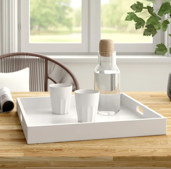 A white rectangular serving tray holds two fluted cups and a glass carafe with a cork stopper on a light wood table.