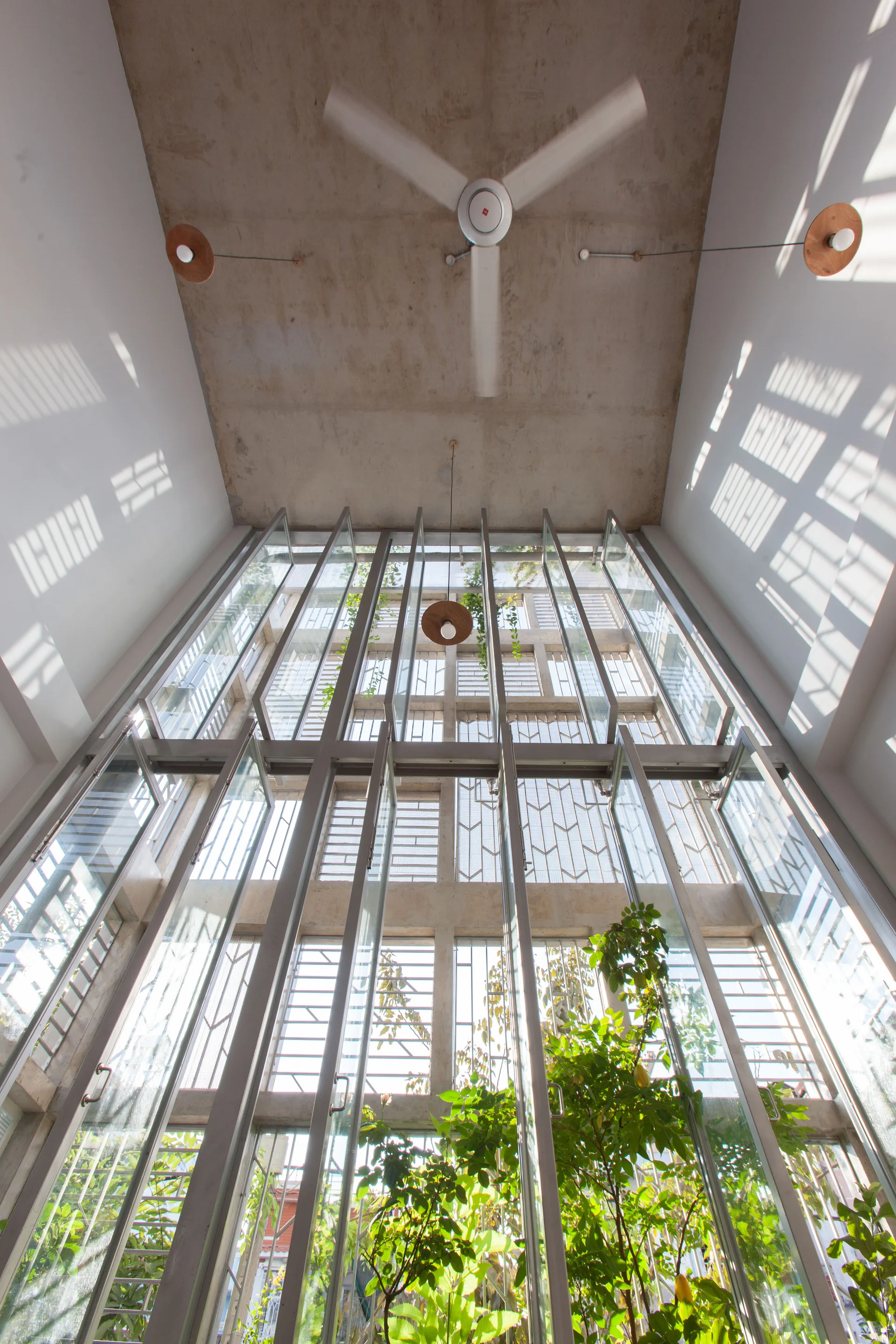 An upward view of a double-height atrium featuring a raw concrete ceiling, white side walls with window shadows, and a towering glass window facade.